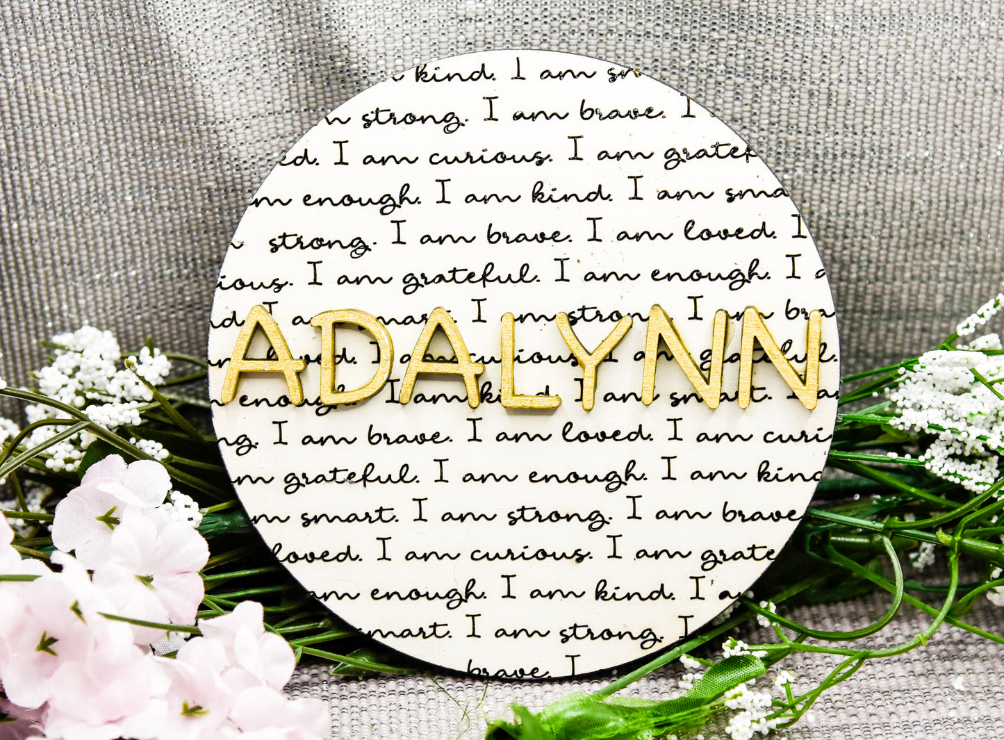 Round wooden name affirmation sign with a custom 3D name on top and engraved positive words like "brave," "kind," and "loved" behind it. Offered in various colors and three sizes, it's perfect for crib name tags, baby announcements, or personalized nursery decor.