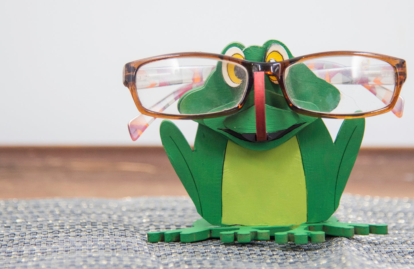 Hand-painted wooden frog-shaped glasses holder with bulging eyes and a flat base to hold eyeglasses. Ideal for desks, nightstands, or gifting to frog lovers and animal fans