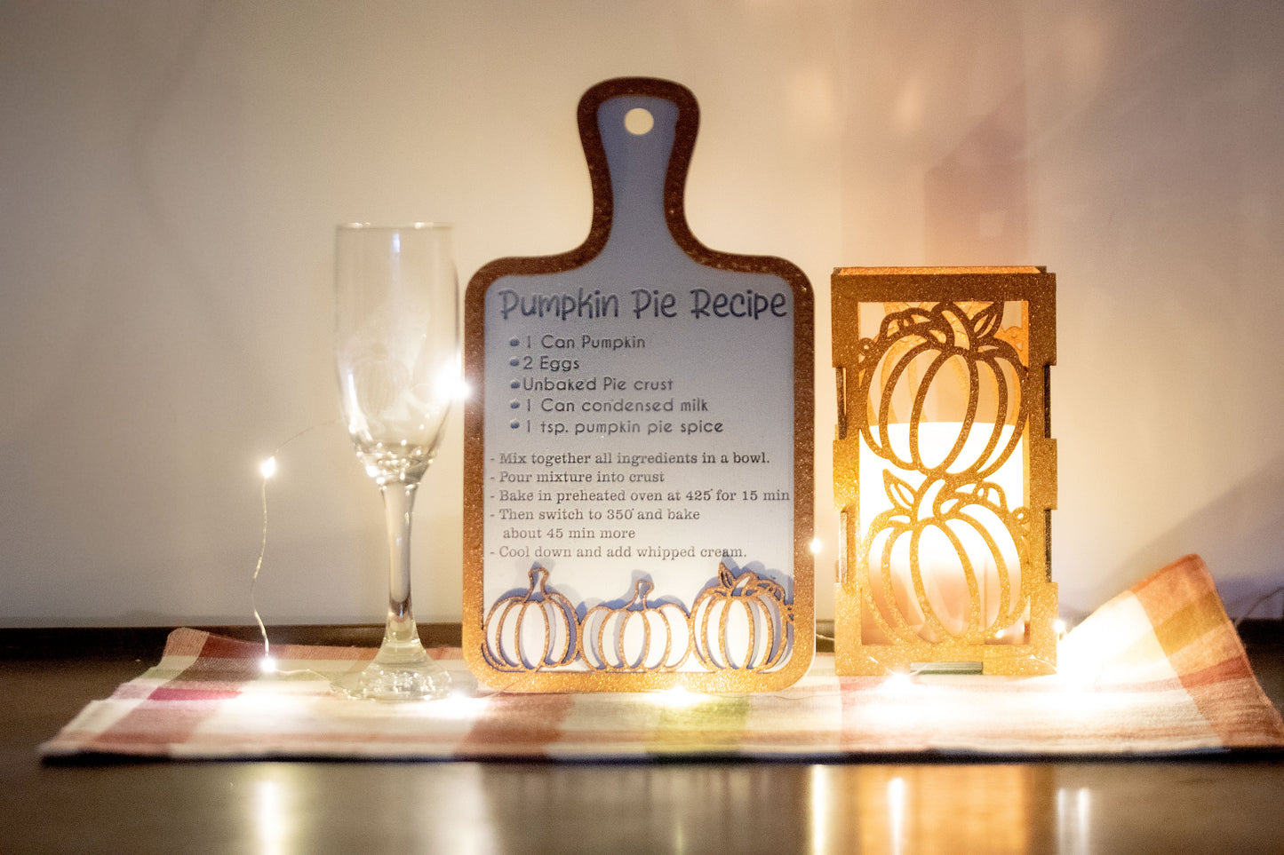 Laser-cut wooden cutting board with engraved pumpkin pie recipe and decorative pumpkins, styled on a fall plaid table runner with pumpkins and wine glass.