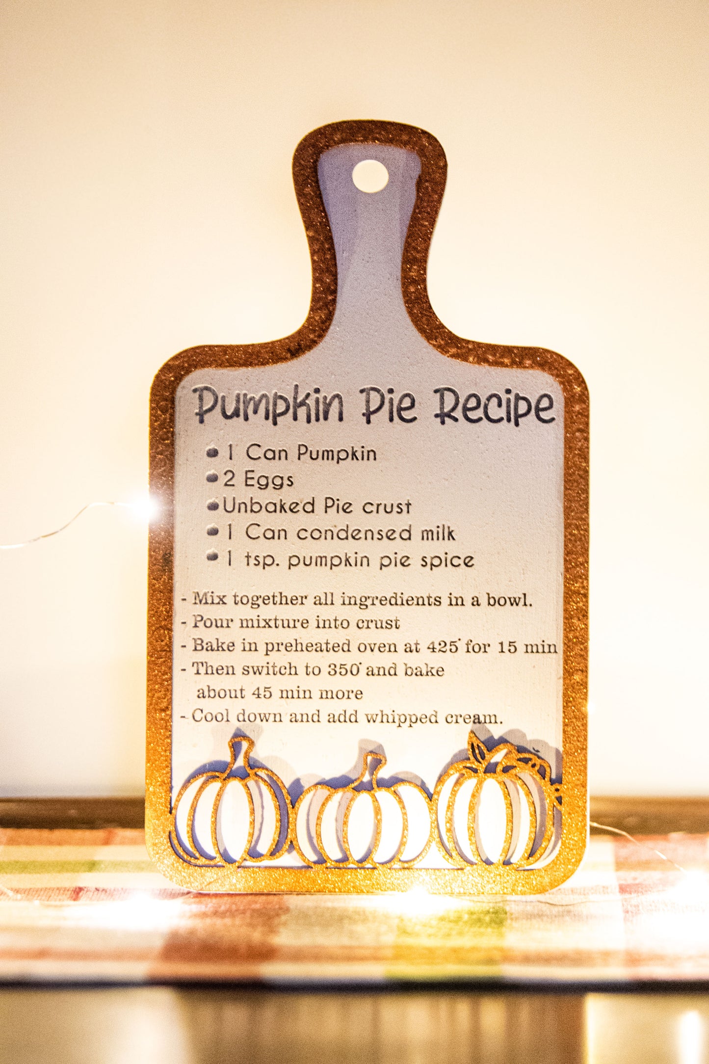 Laser-cut wooden cutting board with engraved pumpkin pie recipe and decorative pumpkins, styled on a fall plaid table runner with pumpkins and wine glass.