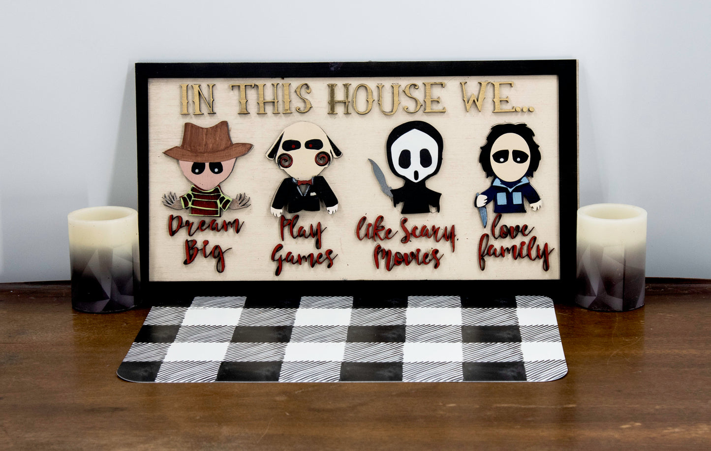 Wooden Halloween sign featuring layered cutout horror movie characters with engraved phrase “In This House,” handcrafted and freestanding, designed for spooky home decor fans.