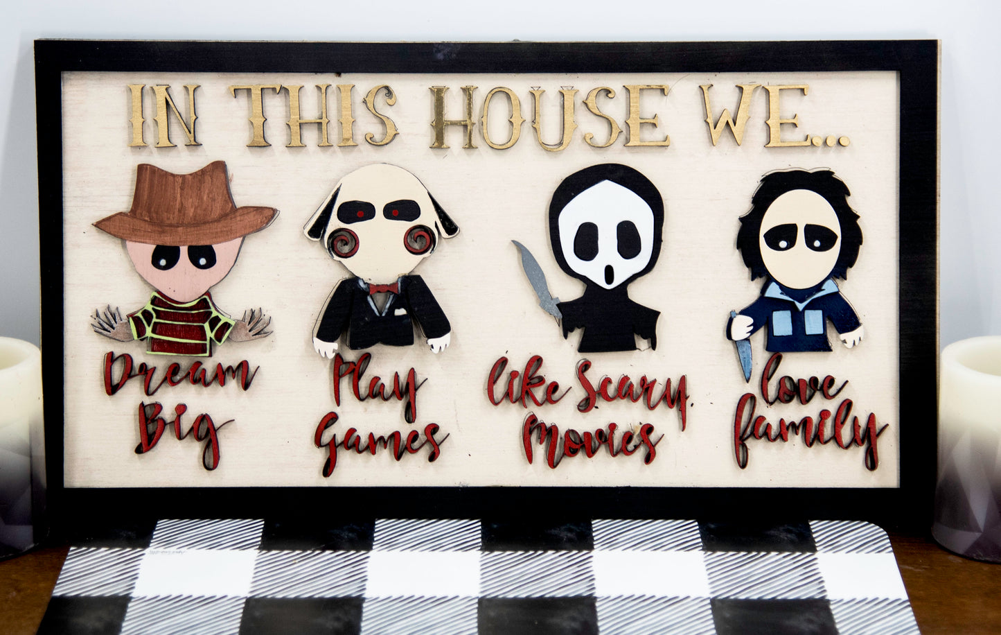 Wooden Halloween sign featuring layered cutout horror movie characters with engraved phrase “In This House,” handcrafted and freestanding, designed for spooky home decor fans.