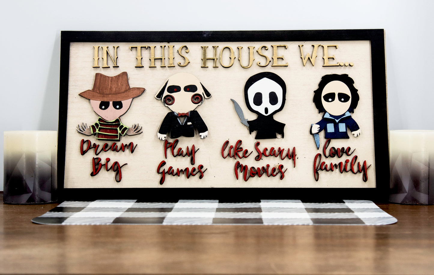 Wooden Halloween sign featuring layered cutout horror movie characters with engraved phrase “In This House,” handcrafted and freestanding, designed for spooky home decor fans.