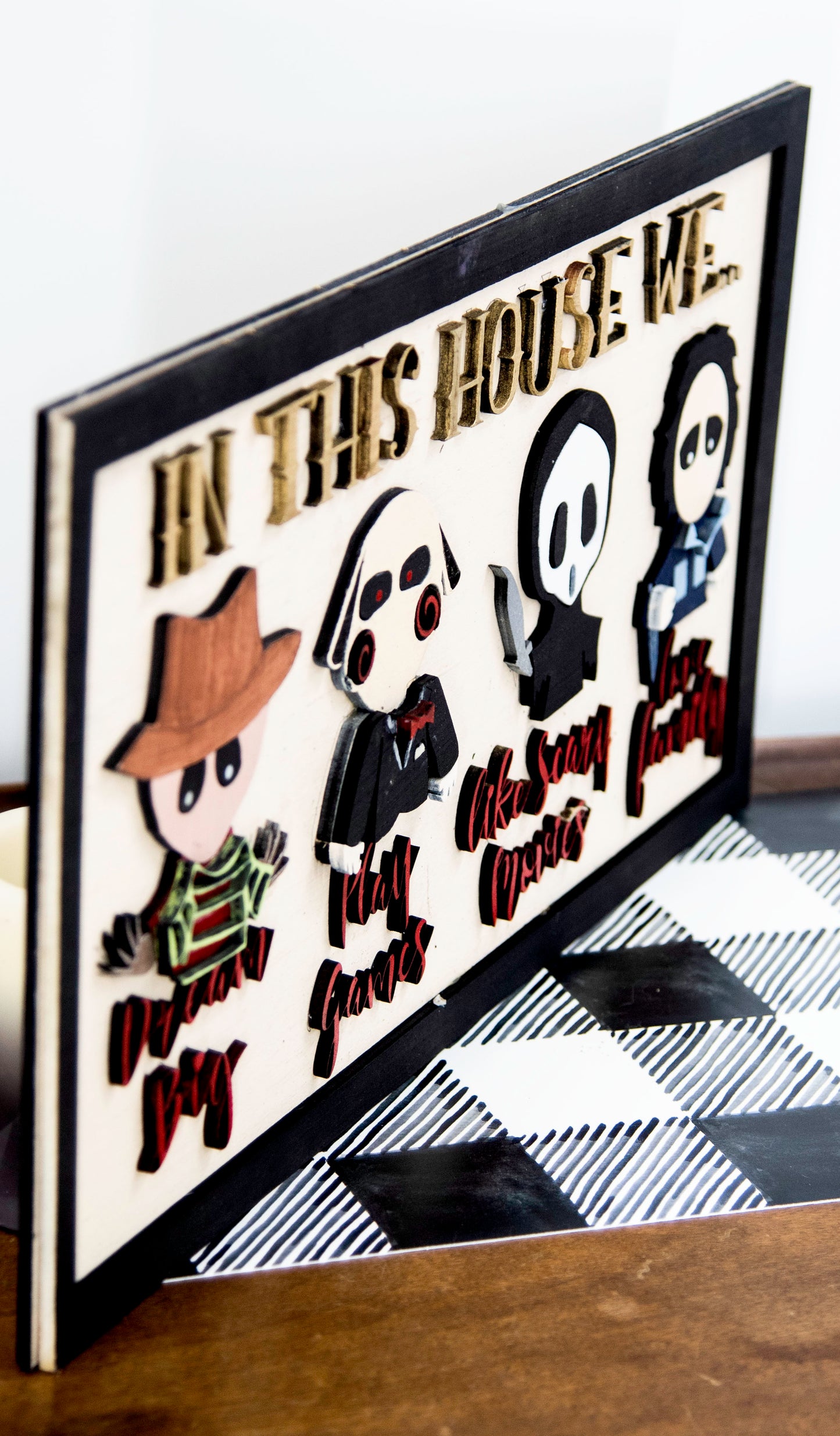 Wooden Halloween sign featuring layered cutout horror movie characters with engraved phrase “In This House,” handcrafted and freestanding, designed for spooky home decor fans.