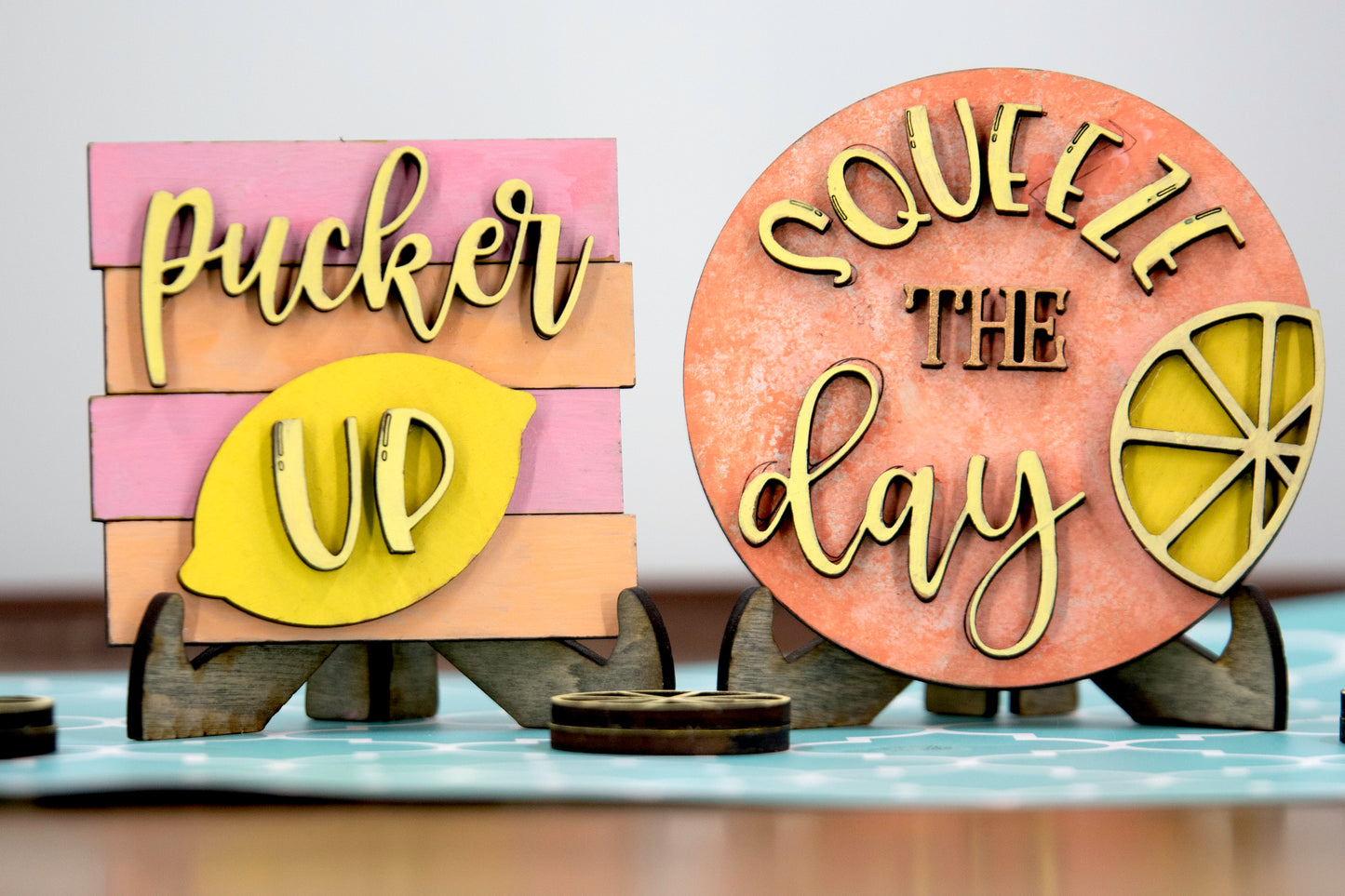 Hand-painted lemonade-themed tiered tray set featuring five wooden decor pieces in pastel pink, yellow, and orange. Includes lemon slice accents, banner flags, and stands for each item. Optional matching wooden tray base available