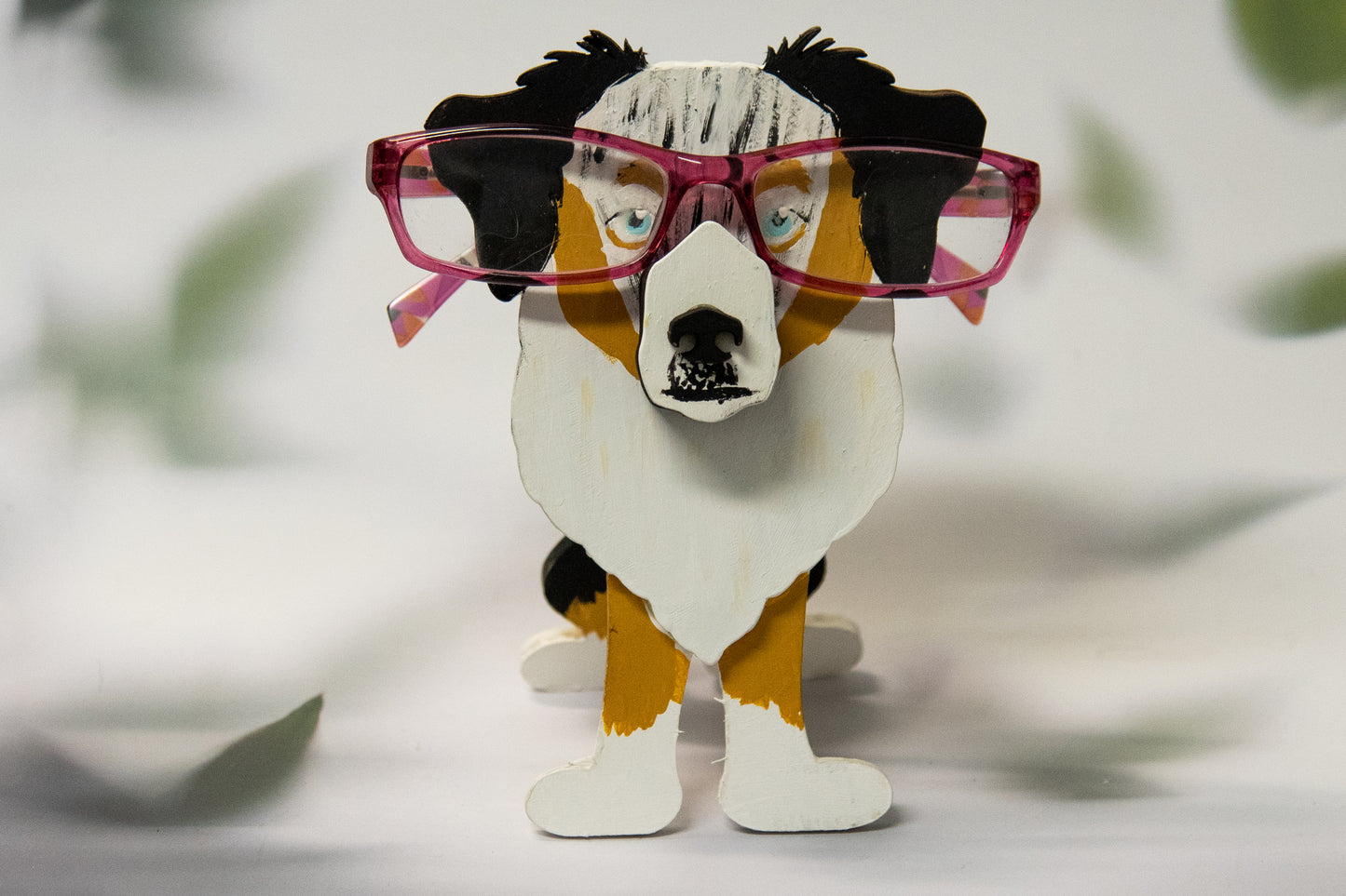 Hand-painted Australian Shepherd eyeglass holder in a sitting dog shape, available in Blue Merle, Red Merle, Black Tri, or custom colors with realistic details, designed to hold glasses on the snout. Cute and functional dog lover gift, hand-crafted and great for desks or nightstands.