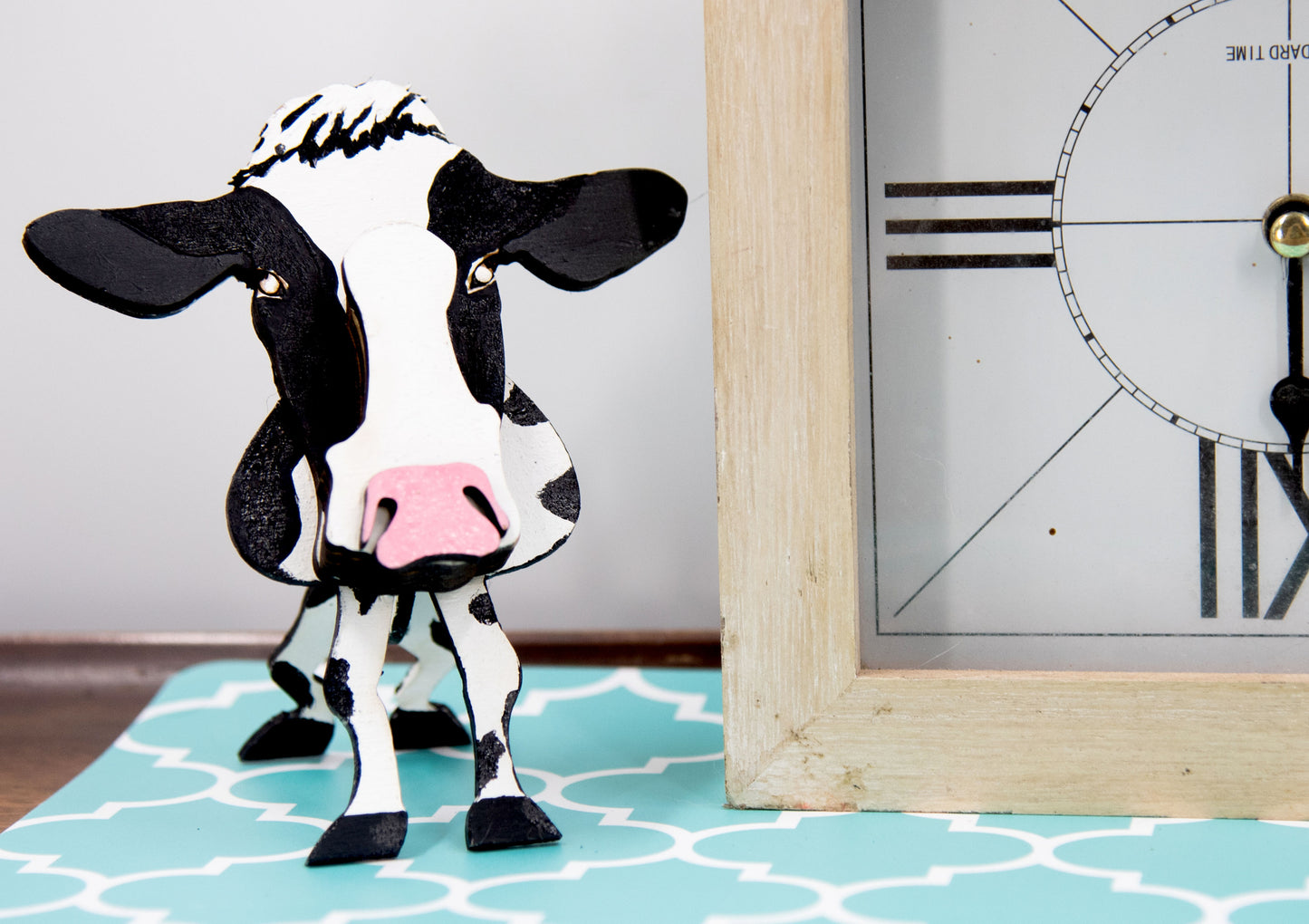 Wooden cow-shaped glasses holder, painted black and white with a layered design, holding a pair of eyeglasses, ideal for farm animal lovers and rustic decor.
