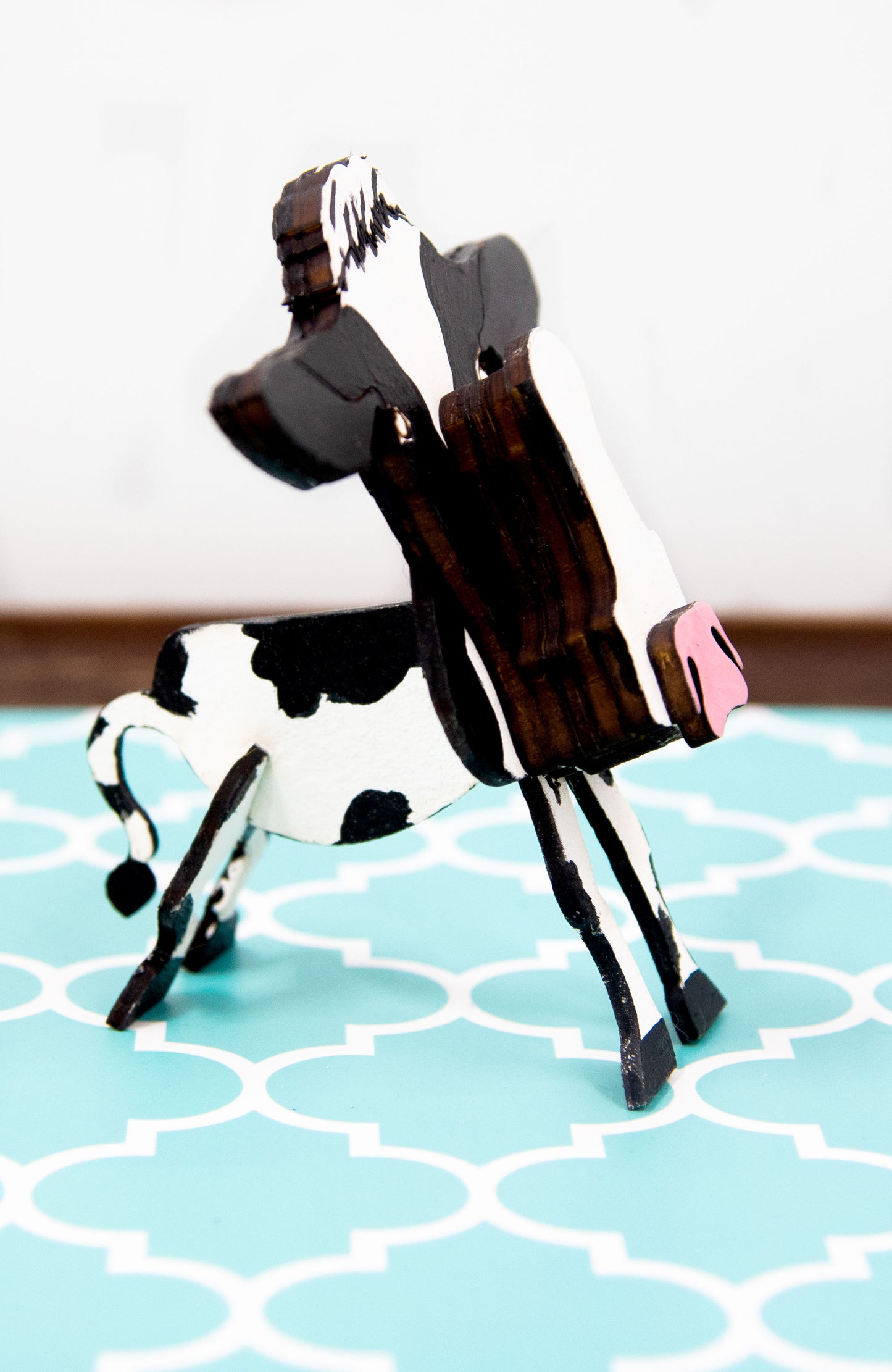 Wooden cow-shaped glasses holder, painted black and white with a layered design, holding a pair of eyeglasses, ideal for farm animal lovers and rustic decor.
