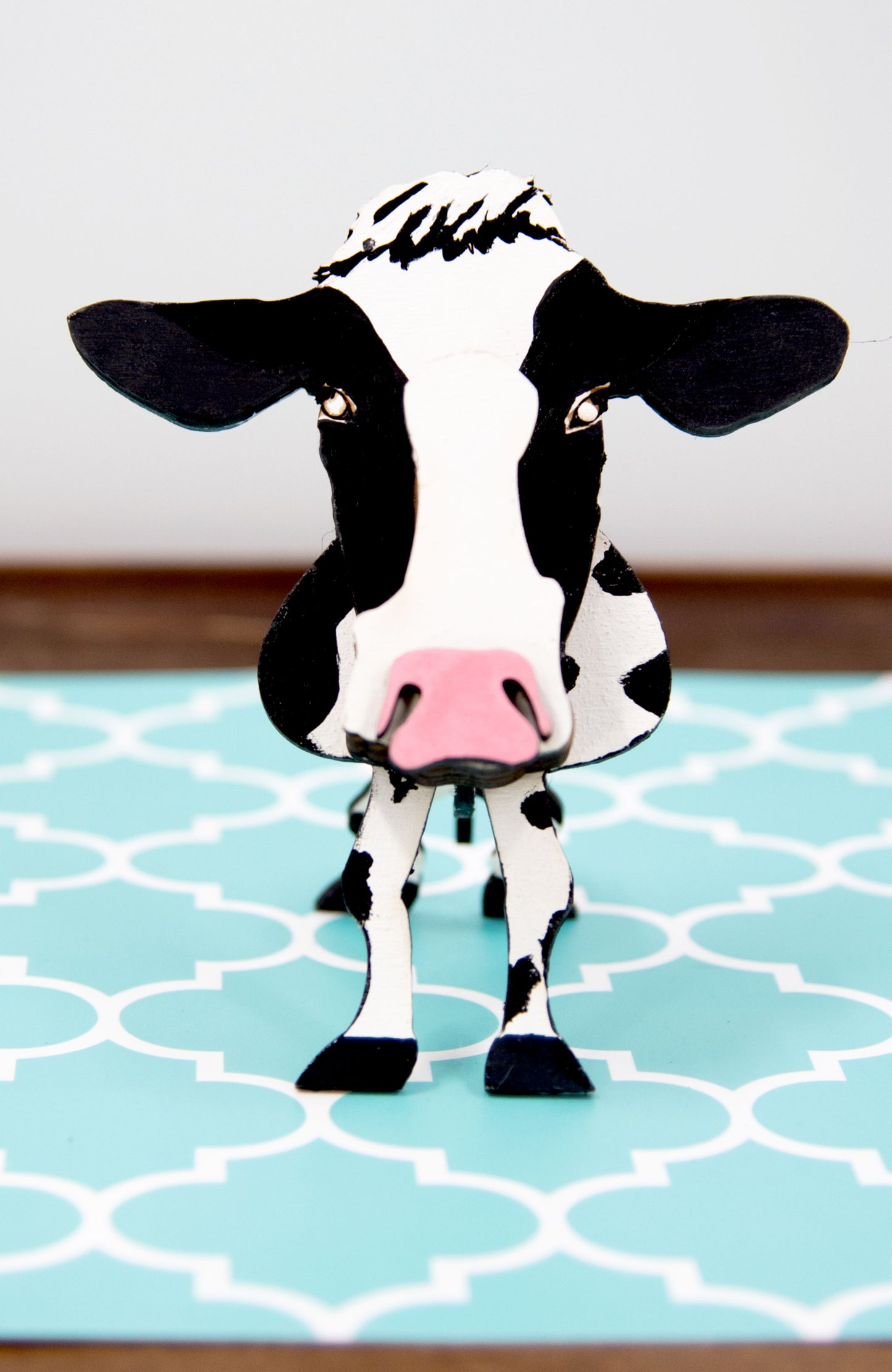 Wooden cow-shaped glasses holder, painted black and white with a layered design, holding a pair of eyeglasses, ideal for farm animal lovers and rustic decor.
