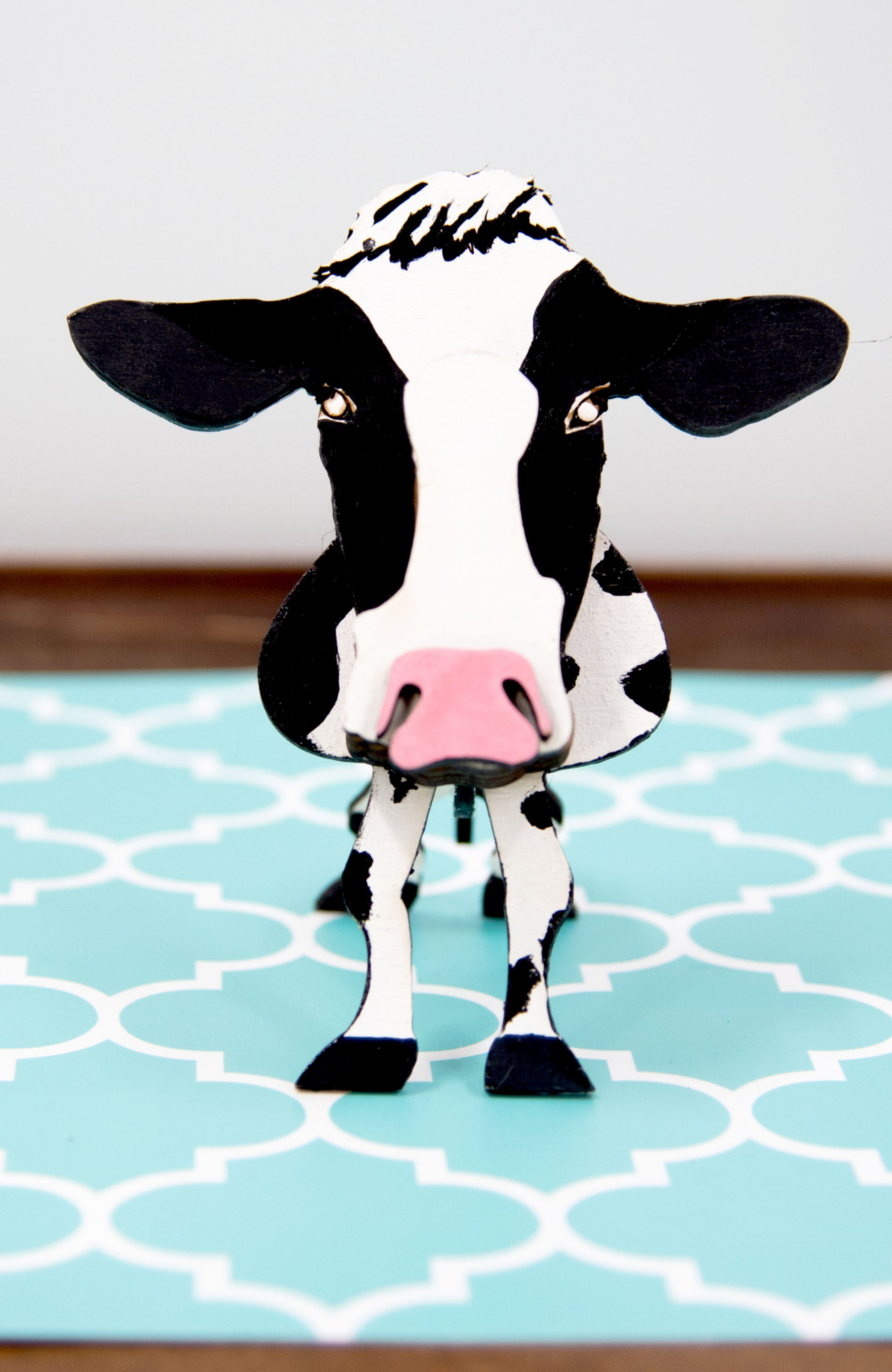 Wooden cow-shaped glasses holder, painted black and white with a layered design, holding a pair of eyeglasses, ideal for farm animal lovers and rustic decor.
