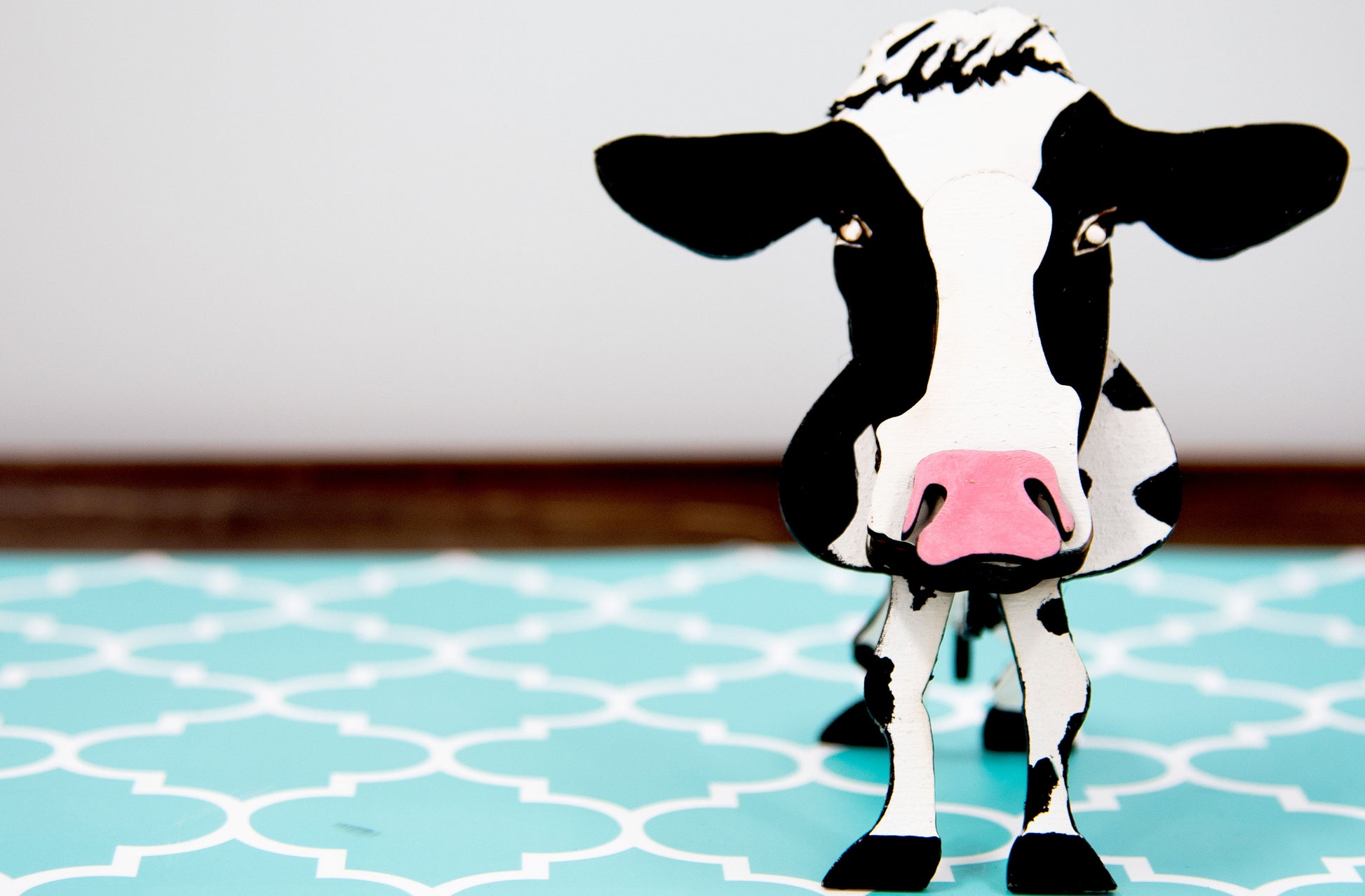 Wooden cow-shaped glasses holder, painted black and white with a layered design, holding a pair of eyeglasses, ideal for farm animal lovers and rustic decor.
