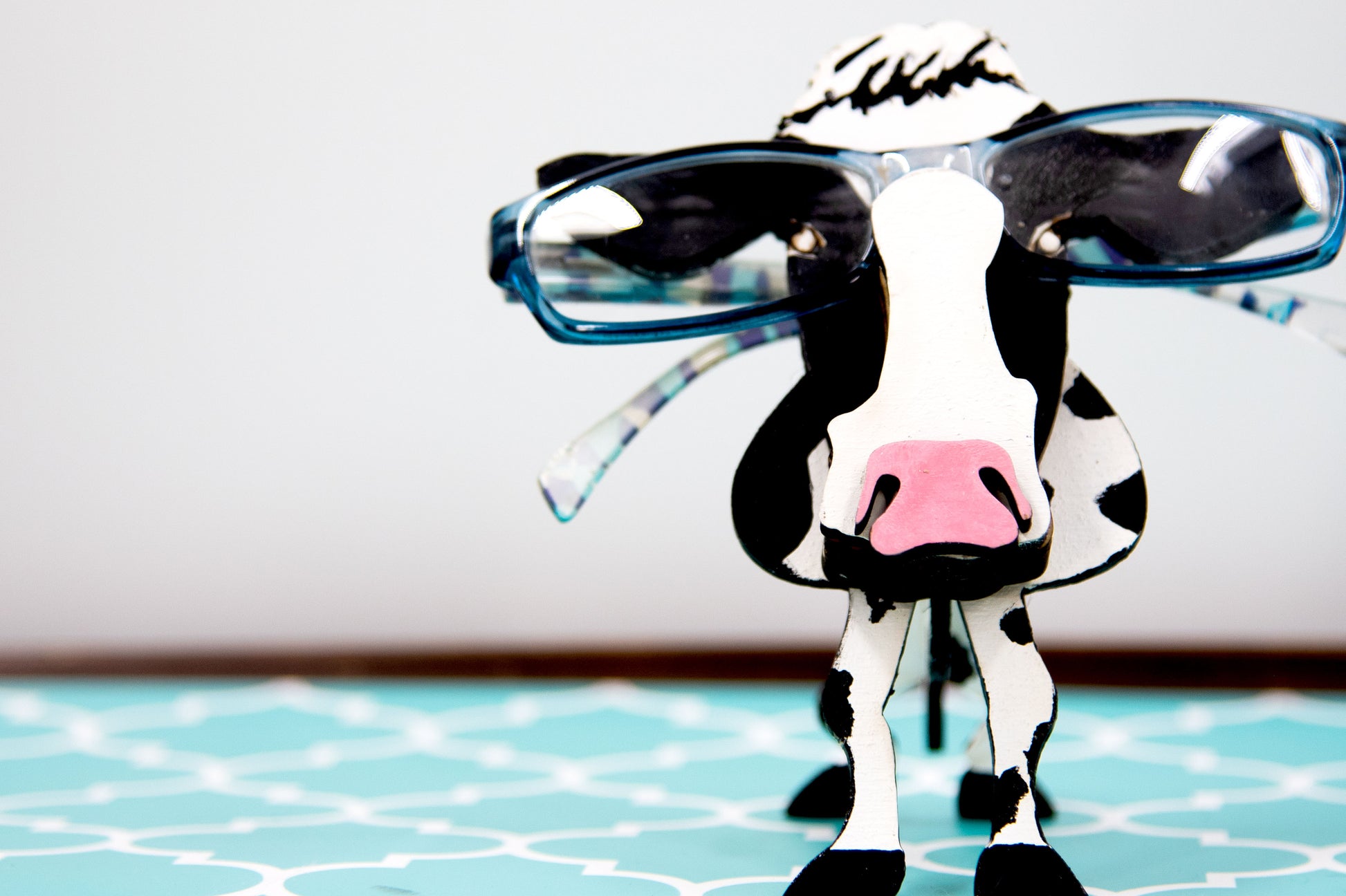 Wooden cow-shaped glasses holder, painted black and white with a layered design, holding a pair of eyeglasses, ideal for farm animal lovers and rustic decor.
