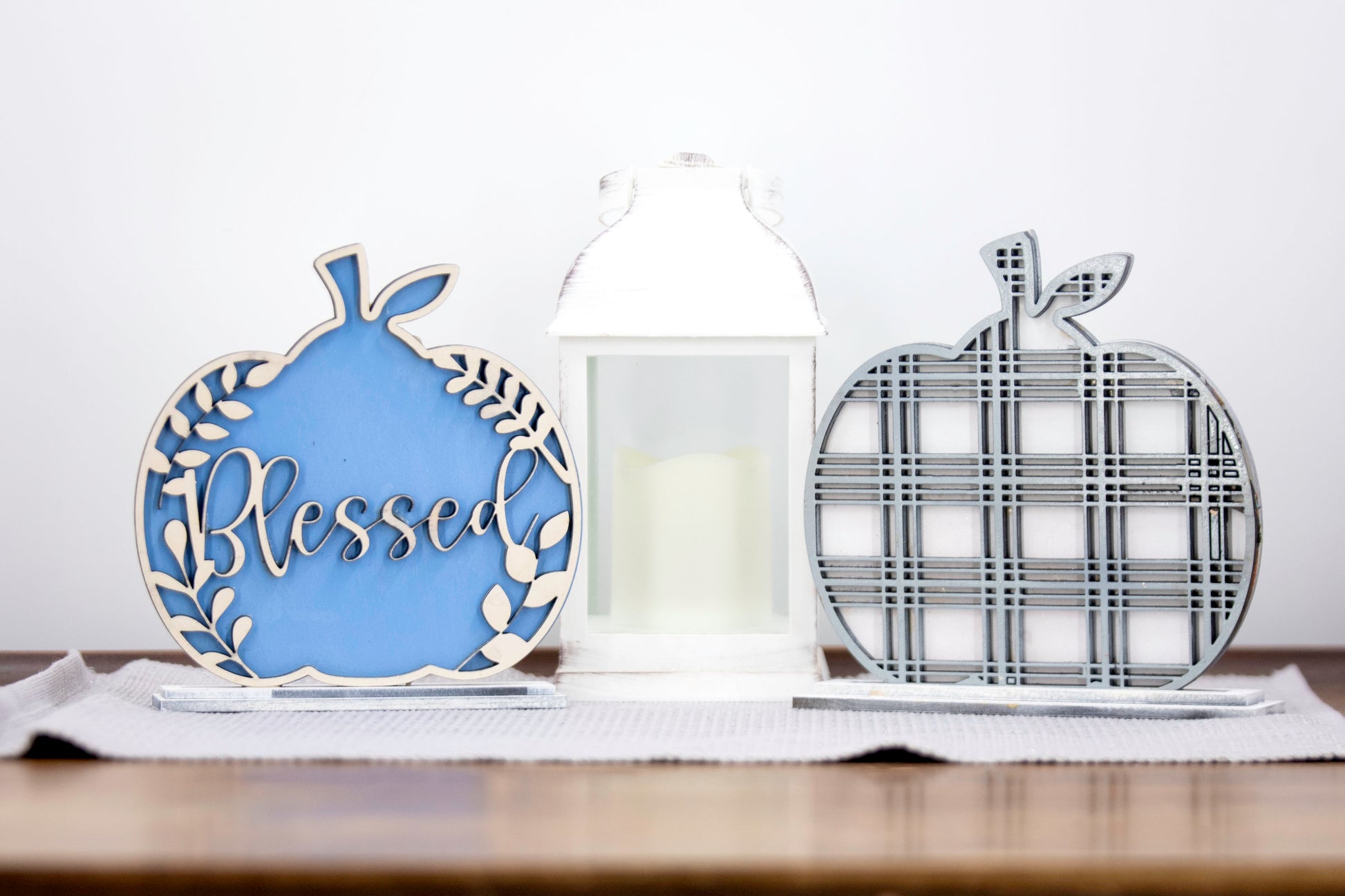 Layered standing wooden pumpkins ranging from 5.5 to 8 inches tall, featuring a solid color background and patterned top layer in assorted fall colors and rustic prints. Some designs include engraved words like 'Blessed' and 'Grateful.' Each pumpkin stands on a wooden base, making them ideal for fall shelf decor, Thanksgiving displays, or farmhouse-style seasonal arrangements.