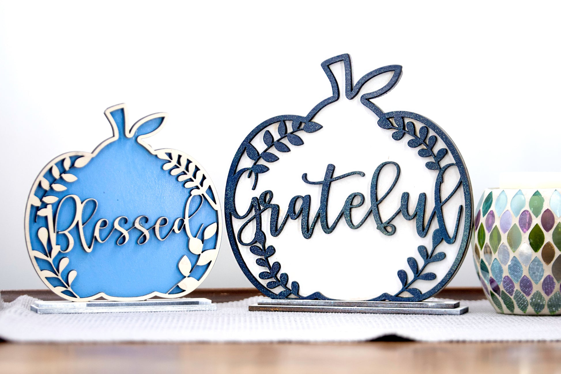 Layered standing wooden pumpkins ranging from 5.5 to 8 inches tall, featuring a solid color background and patterned top layer in assorted fall colors and rustic prints. Some designs include engraved words like 'Blessed' and 'Grateful.' Each pumpkin stands on a wooden base, making them ideal for fall shelf decor, Thanksgiving displays, or farmhouse-style seasonal arrangements.