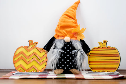 Layered standing wooden pumpkins ranging from 5.5 to 8 inches tall, featuring a solid color background and patterned top layer in assorted fall colors and rustic prints. Some designs include engraved words like 'Blessed' and 'Grateful.' Each pumpkin stands on a wooden base, making them ideal for fall shelf decor, Thanksgiving displays, or farmhouse-style seasonal arrangements.