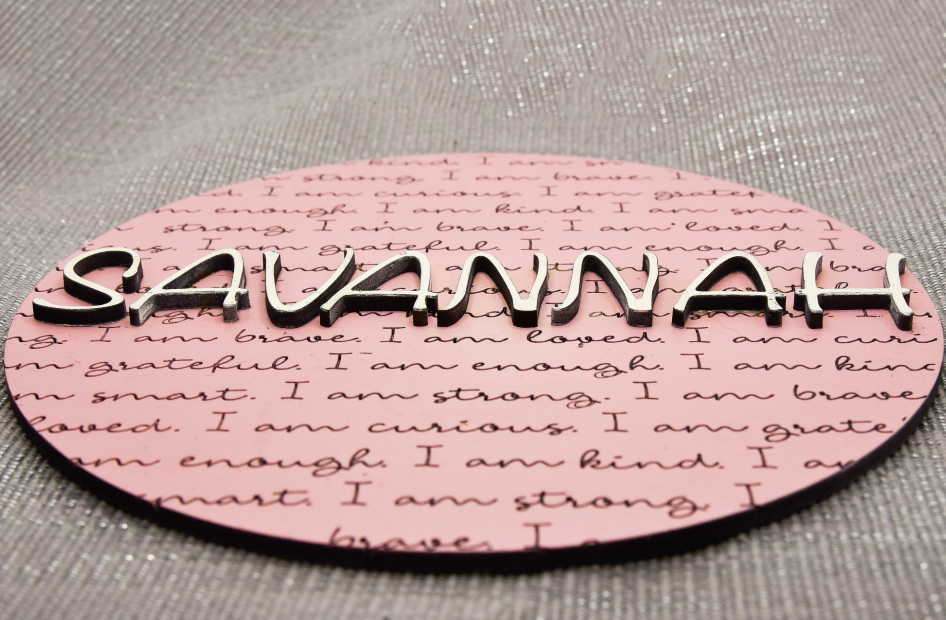Round wooden name affirmation sign with a custom 3D name on top and engraved positive words like "brave," "kind," and "loved" behind it. Offered in various colors and three sizes, it's perfect for crib name tags, baby announcements, or personalized nursery decor.