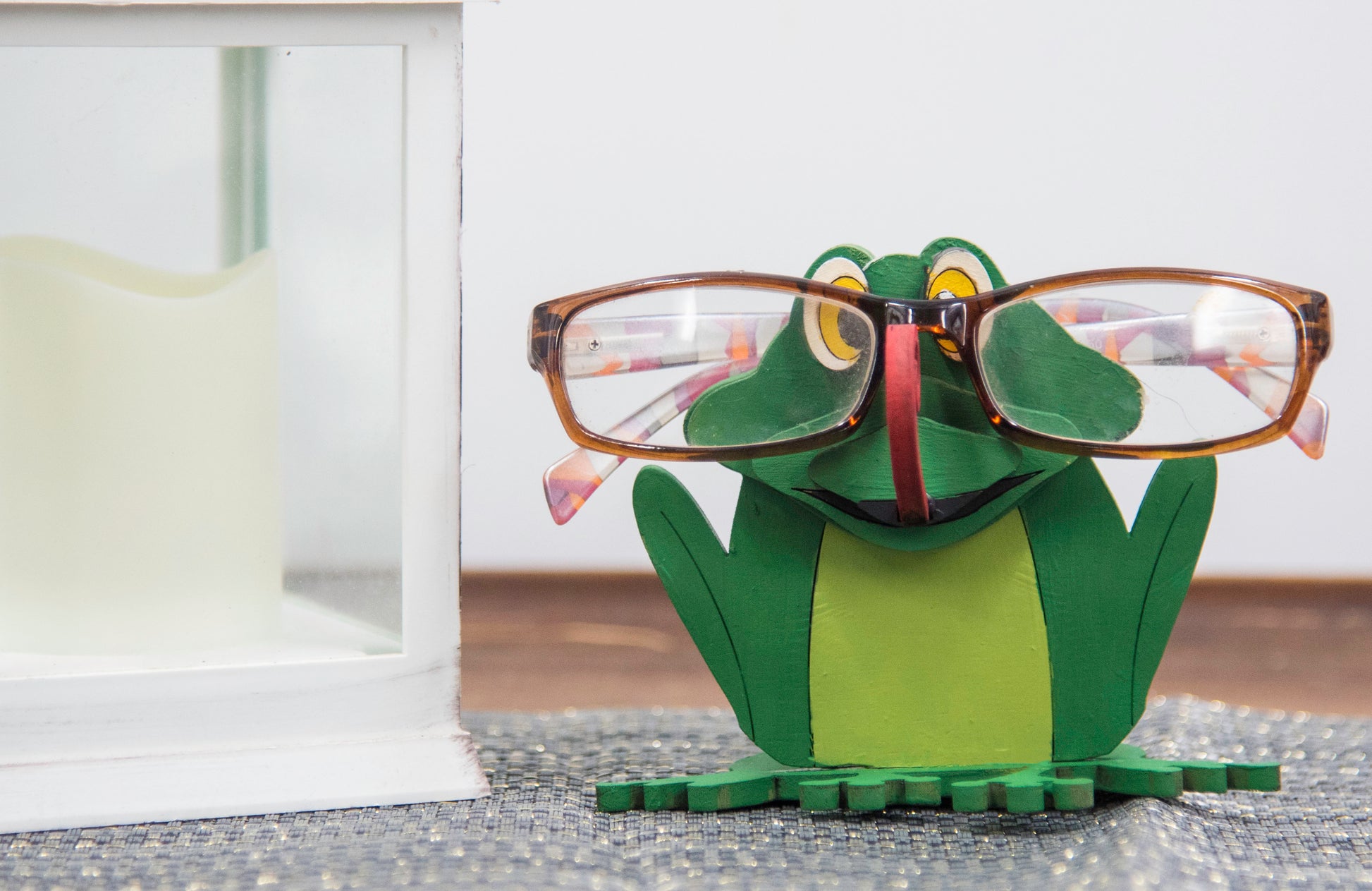 Hand-painted wooden frog-shaped glasses holder with bulging eyes and a flat base to hold eyeglasses. Ideal for desks, nightstands, or gifting to frog lovers and animal fans