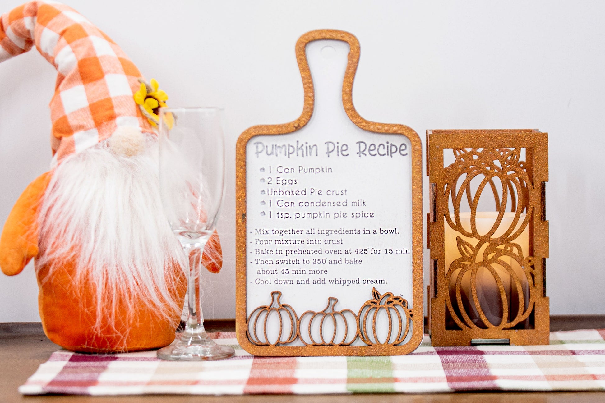 Laser-cut wooden cutting board with engraved pumpkin pie recipe and decorative pumpkins, styled on a fall plaid table runner with pumpkins and wine glass.
