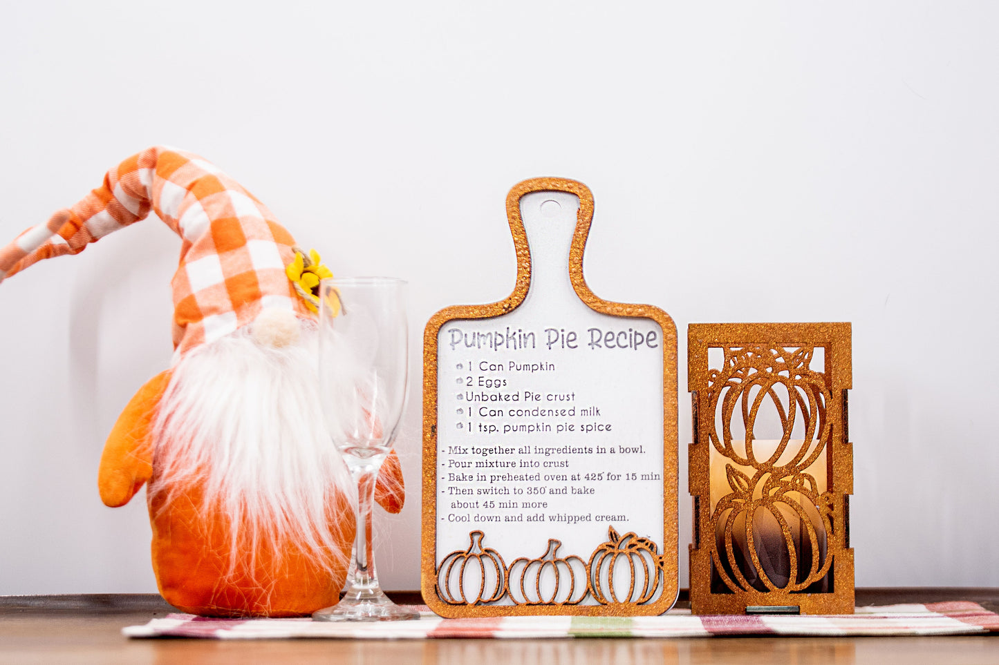 Laser-cut wooden cutting board with engraved pumpkin pie recipe and decorative pumpkins, styled on a fall plaid table runner with pumpkins and wine glass.
