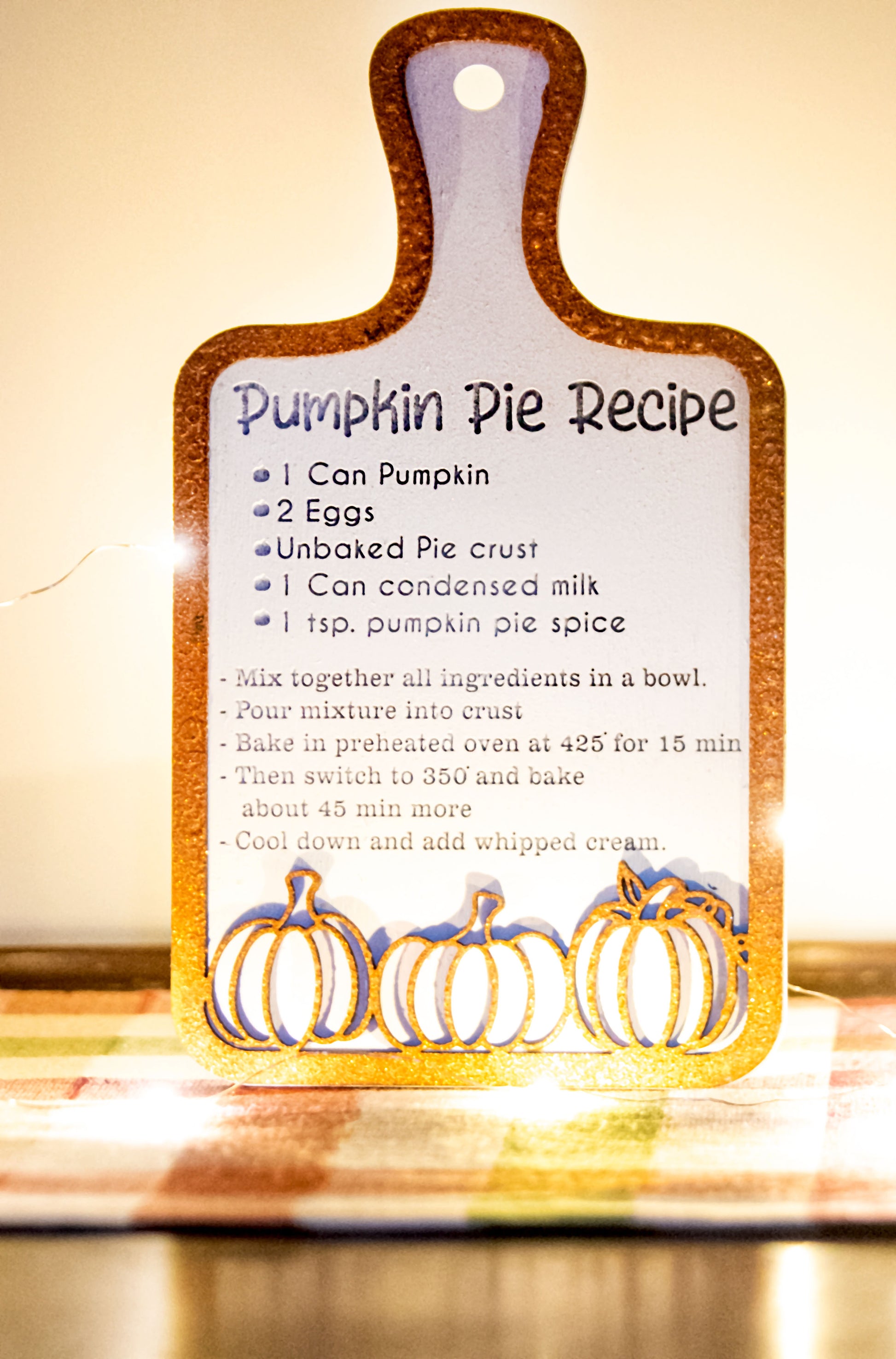 Laser-cut wooden cutting board with engraved pumpkin pie recipe and decorative pumpkins, styled on a fall plaid table runner with pumpkins and wine glass.

