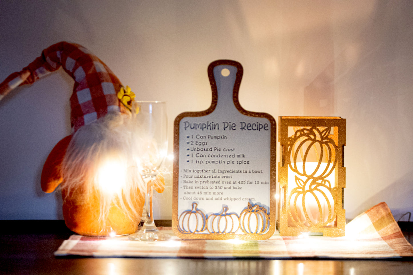 Laser-cut wooden cutting board with engraved pumpkin pie recipe and decorative pumpkins, styled on a fall plaid table runner with pumpkins and wine glass.
