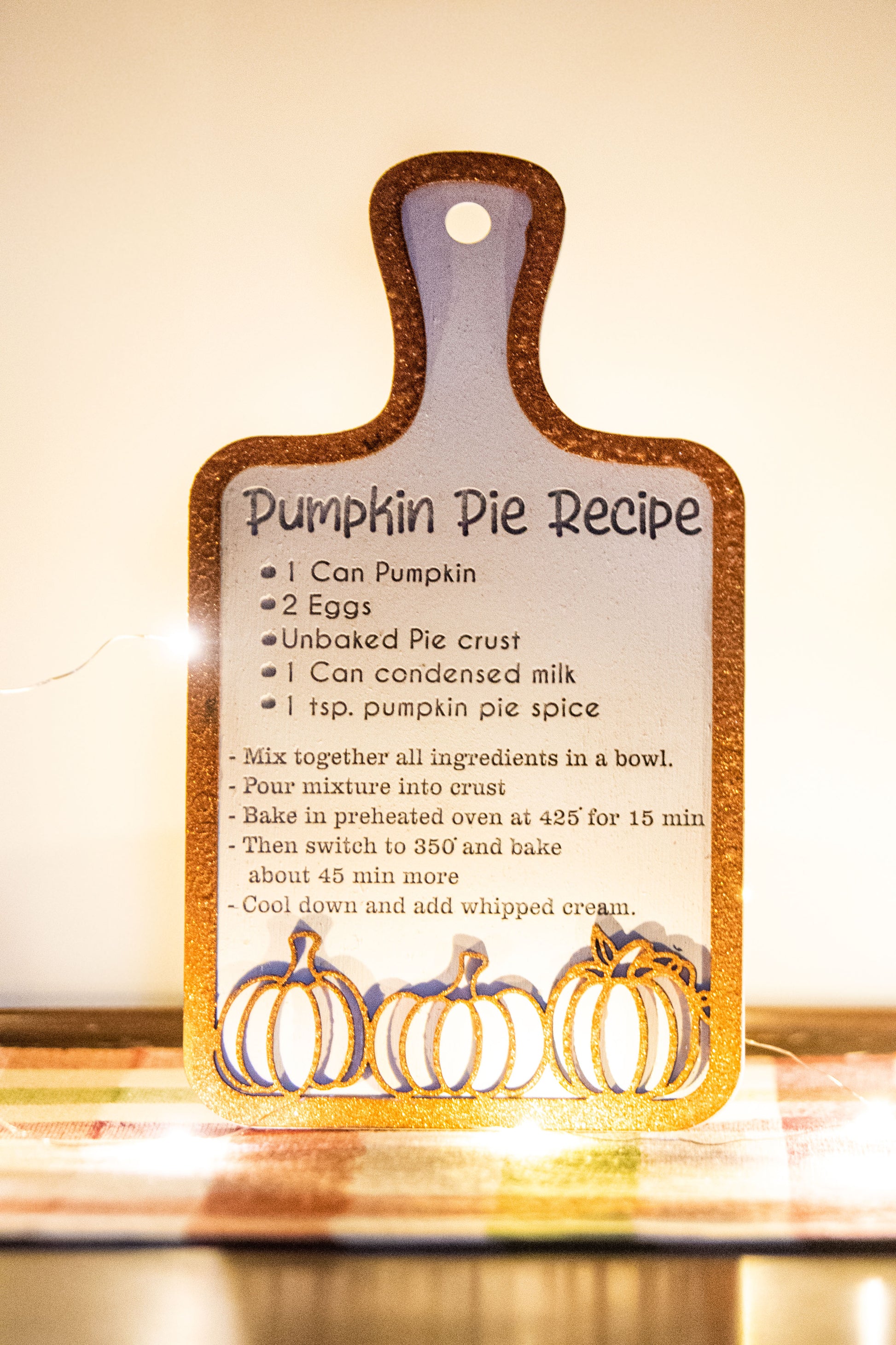 Laser-cut wooden cutting board with engraved pumpkin pie recipe and decorative pumpkins, styled on a fall plaid table runner with pumpkins and wine glass.
