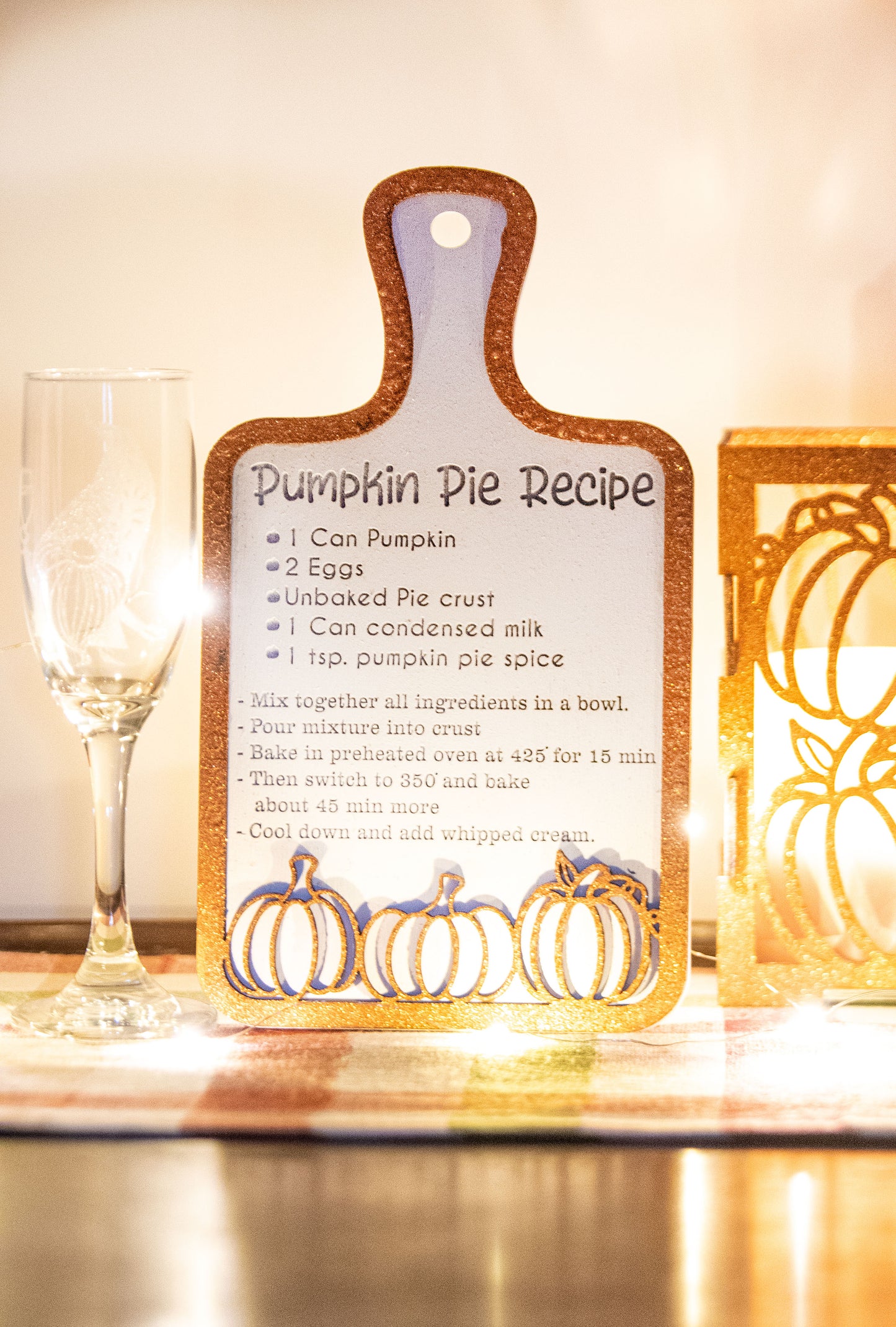 Laser-cut wooden cutting board with engraved pumpkin pie recipe and decorative pumpkins, styled on a fall plaid table runner with pumpkins and wine glass.
