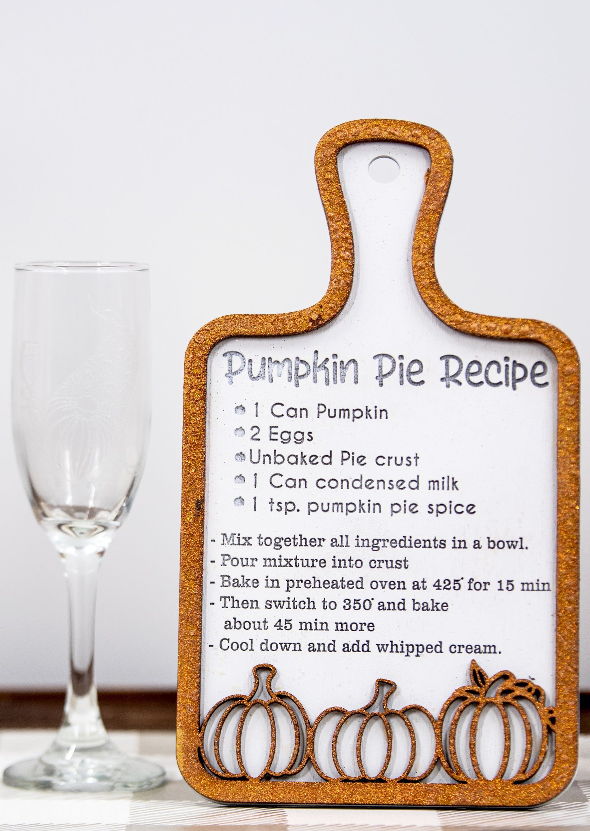 Laser-cut wooden cutting board with engraved pumpkin pie recipe and decorative pumpkins, styled on a fall plaid table runner with pumpkins and wine glass.
