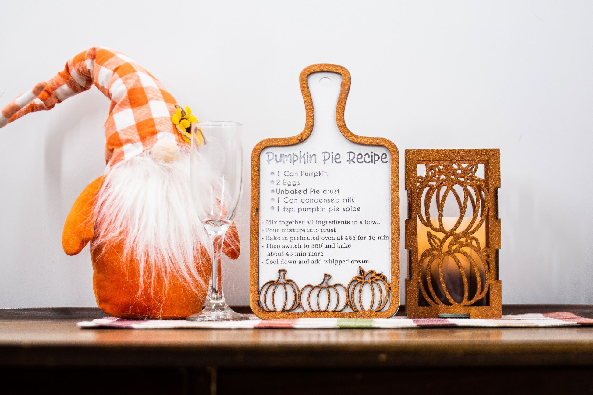 Laser-cut wooden cutting board with engraved pumpkin pie recipe and decorative pumpkins, styled on a fall plaid table runner with pumpkins and wine glass.
