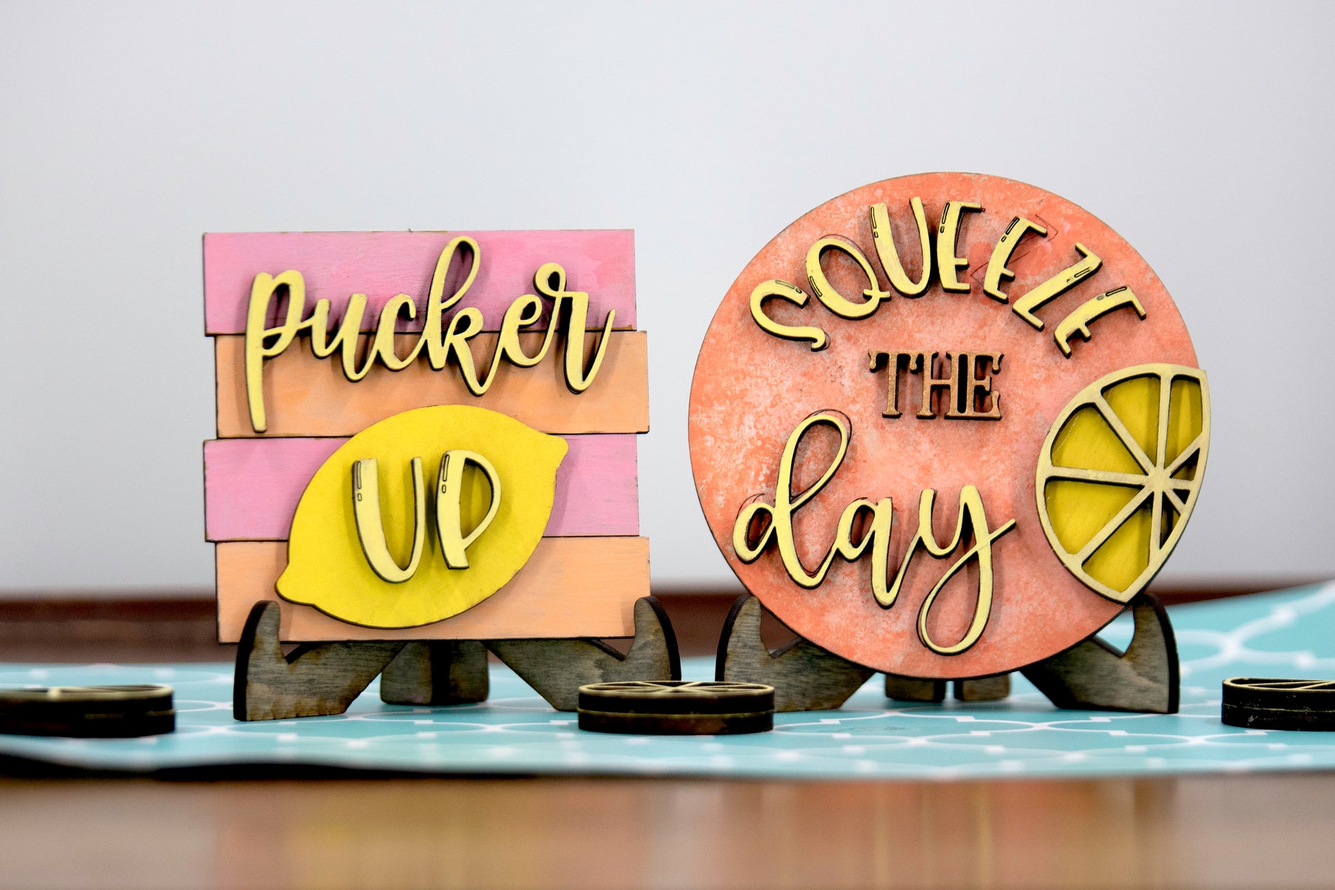 Hand-painted lemonade-themed tiered tray set featuring five wooden decor pieces in pastel pink, yellow, and orange. Includes lemon slice accents, banner flags, and stands for each item. Optional matching wooden tray base available