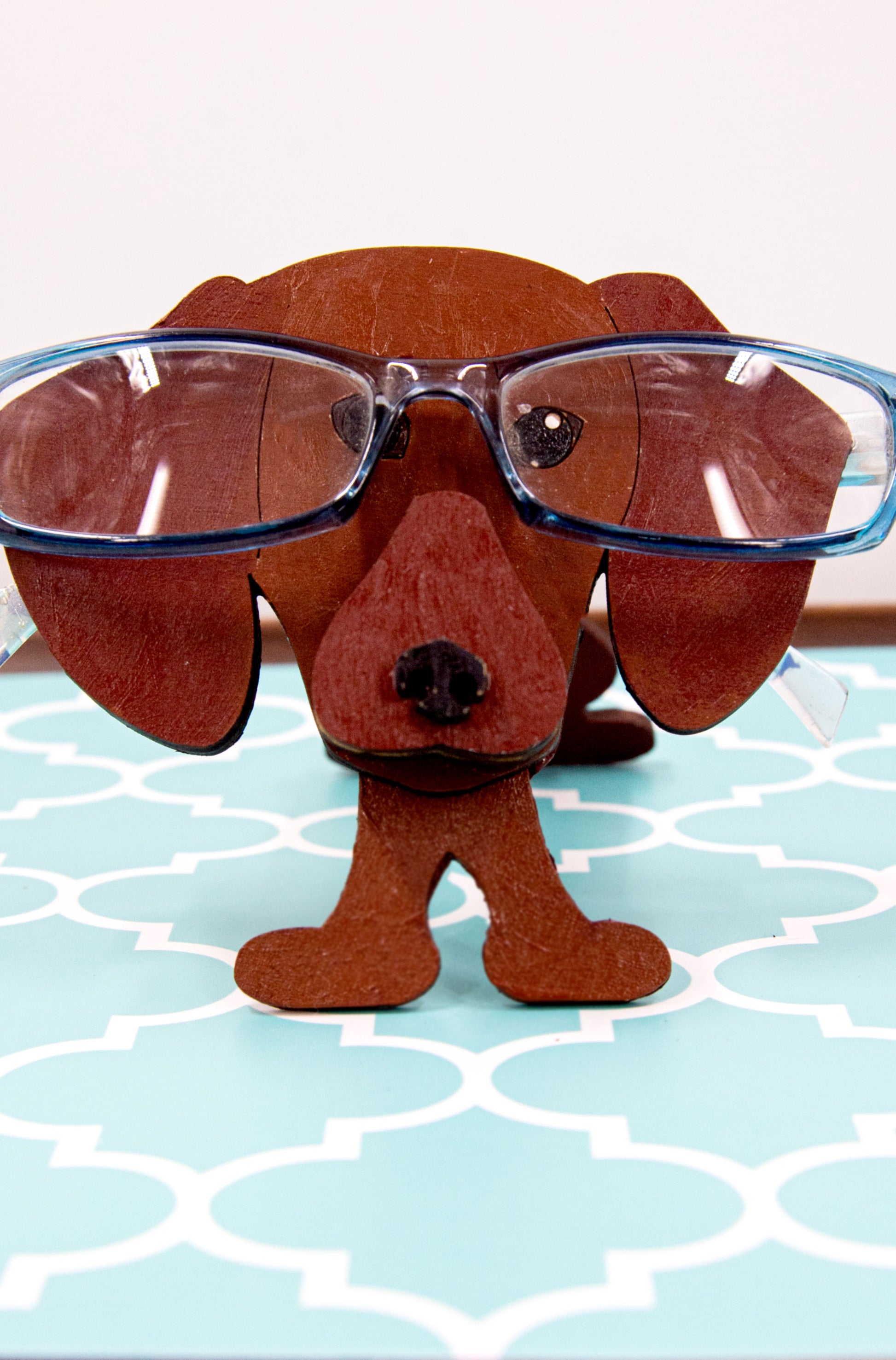 Handcrafted small wooden glasses holder in the shape of a Dachshund, featuring a painted dog design with carved detail and a curved snout to hold eyeglasses securely. A compact and charming gift for dog lovers, especially fans of wiener dogs, and perfect for display on a nightstand, office desk, or bookshelf.