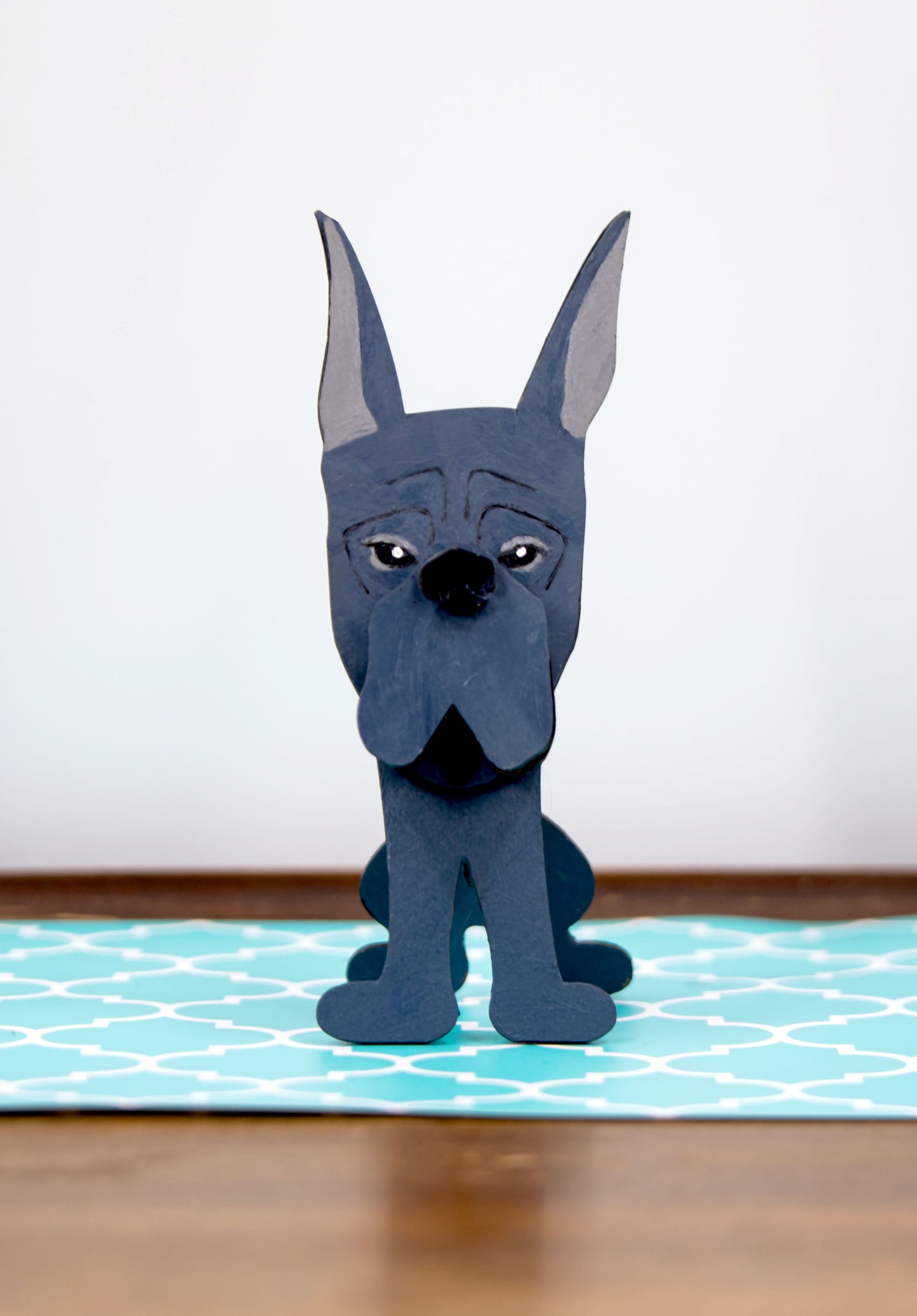 A handcrafted wooden Great Dane eyeglasses holder designed to resemble the iconic breed, available with floppy or docked ears. Comes in black, blue, fawn, or detailed mantle coloring. Floppy ear version measures 6.35" tall by 4.35" wide; docked ear version stands 8.5" tall by 3.15" wide. Perfect for organizing glasses on desks or nightstands, and makes a great gift for Great Dane lovers.