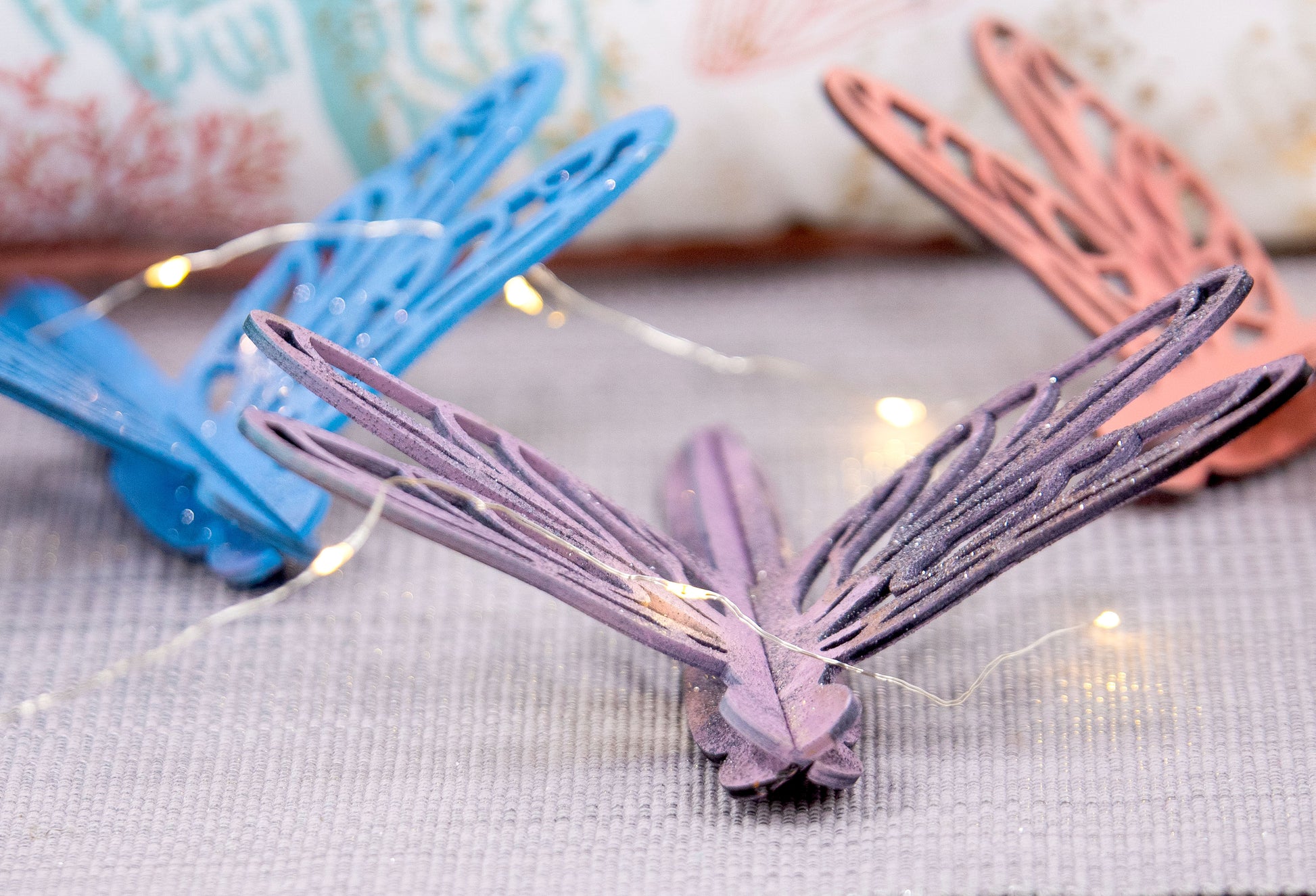 Colorful wooden dragonfly shelf sitters in rustic painted finishes, each shaped with wings and body details, perfect for whimsical spring or summer decor on mantels, shelves, or tiered trays.