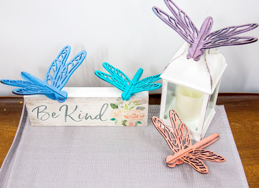 Colorful wooden dragonfly shelf sitters in rustic painted finishes, each shaped with wings and body details, perfect for whimsical spring or summer decor on mantels, shelves, or tiered trays.
