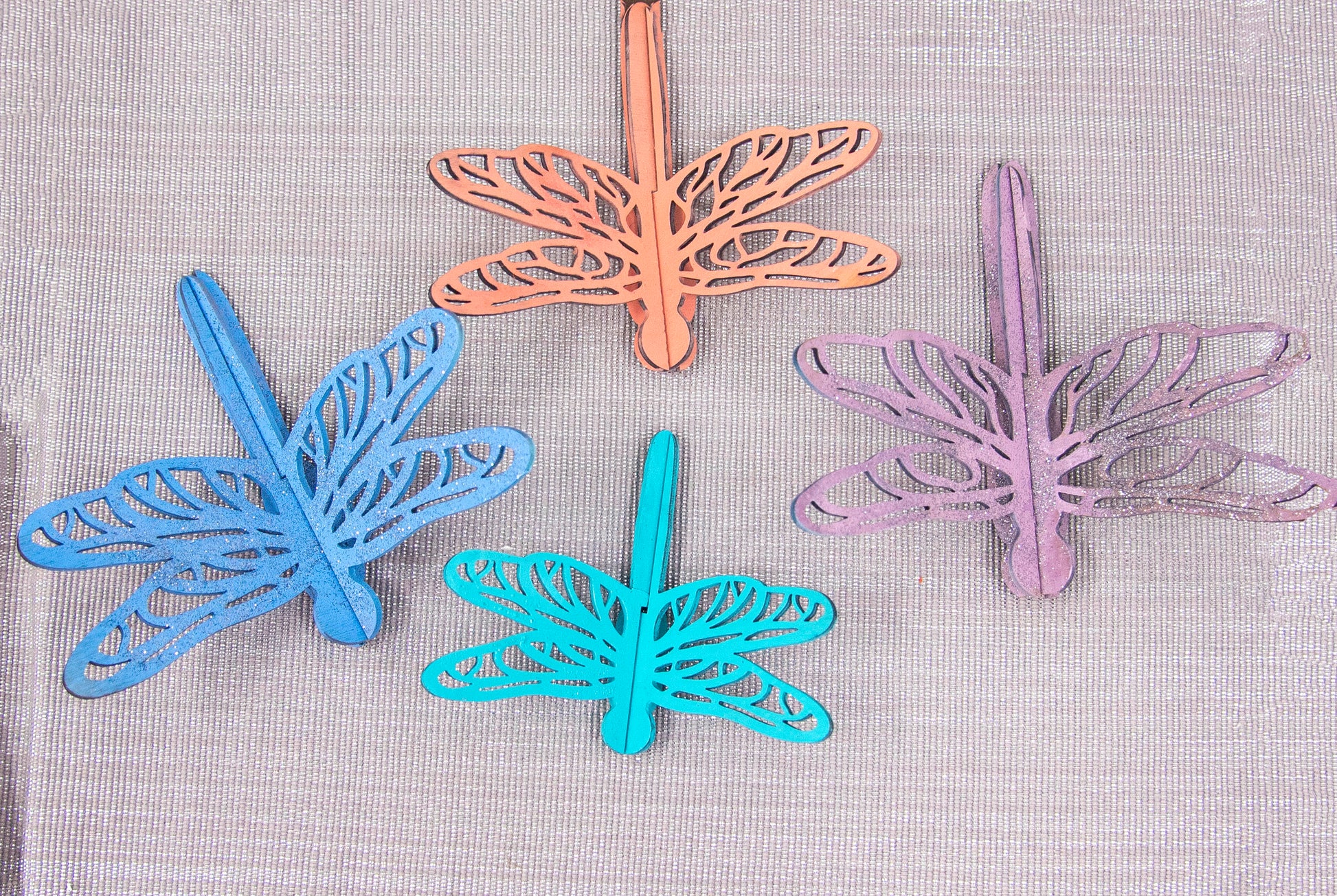 Colorful wooden dragonfly shelf sitters in rustic painted finishes, each shaped with wings and body details, perfect for whimsical spring or summer decor on mantels, shelves, or tiered trays.
