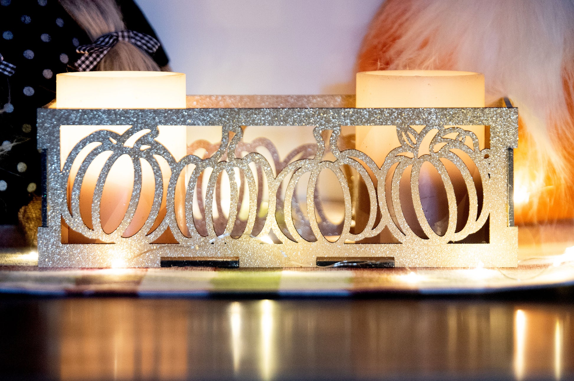 et of three intricately designed metal and wood pumpkin candle holders displayed on a checkered fall table runner. The set includes a tall rectangular lantern, a horizontal centerpiece tray, and a small square holder, each featuring layered pumpkin cutouts that beautifully glow with the warm light of tea candles inside—perfect for cozy fall, Thanksgiving, or farmhouse-style decor.