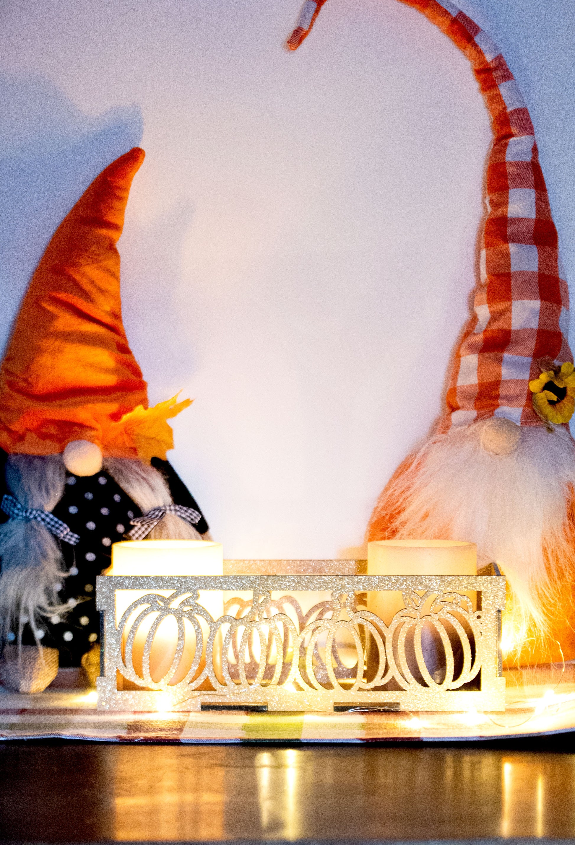et of three intricately designed metal and wood pumpkin candle holders displayed on a checkered fall table runner. The set includes a tall rectangular lantern, a horizontal centerpiece tray, and a small square holder, each featuring layered pumpkin cutouts that beautifully glow with the warm light of tea candles inside—perfect for cozy fall, Thanksgiving, or farmhouse-style decor.