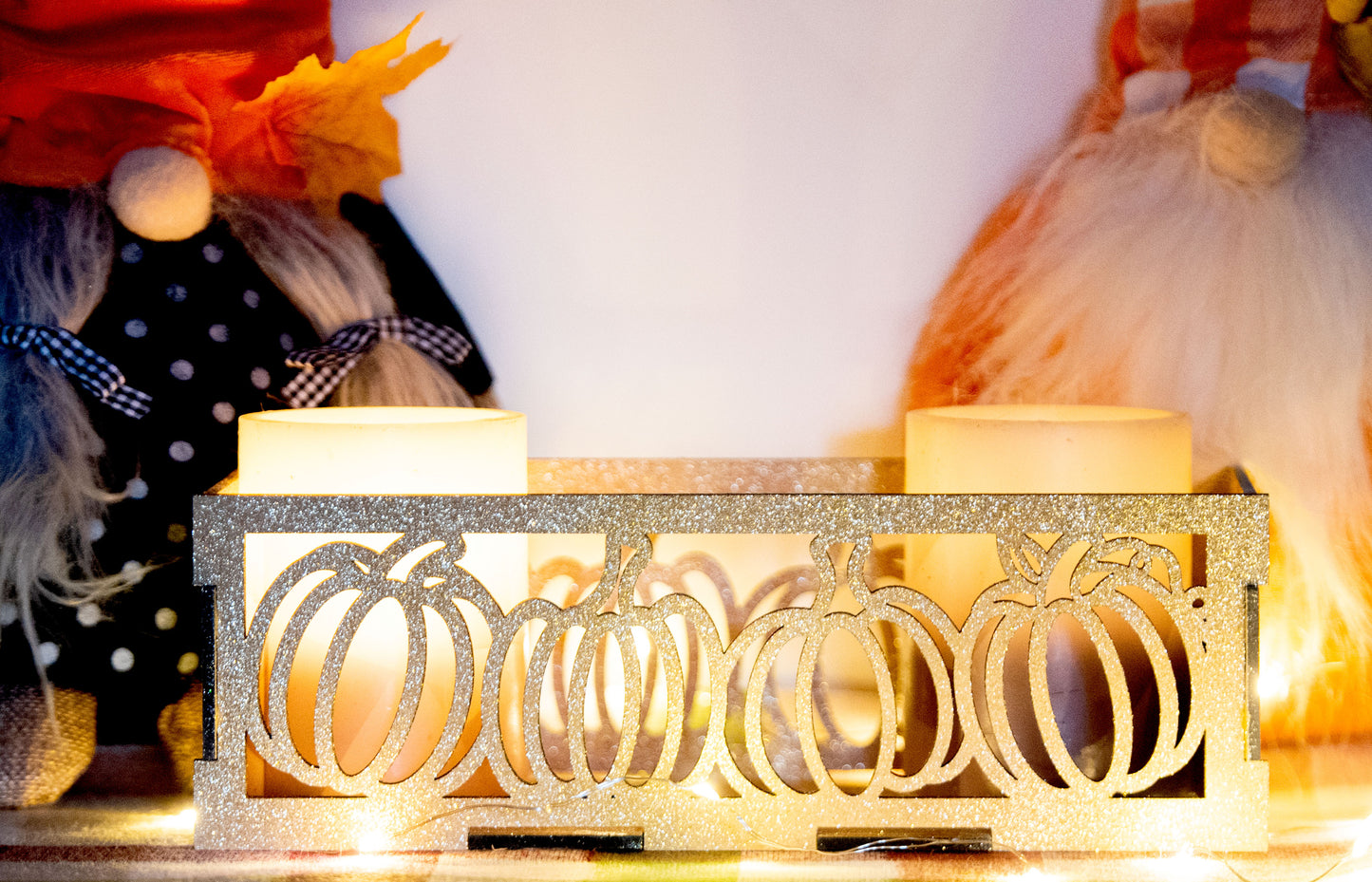 et of three intricately designed metal and wood pumpkin candle holders displayed on a checkered fall table runner. The set includes a tall rectangular lantern, a horizontal centerpiece tray, and a small square holder, each featuring layered pumpkin cutouts that beautifully glow with the warm light of tea candles inside—perfect for cozy fall, Thanksgiving, or farmhouse-style decor.