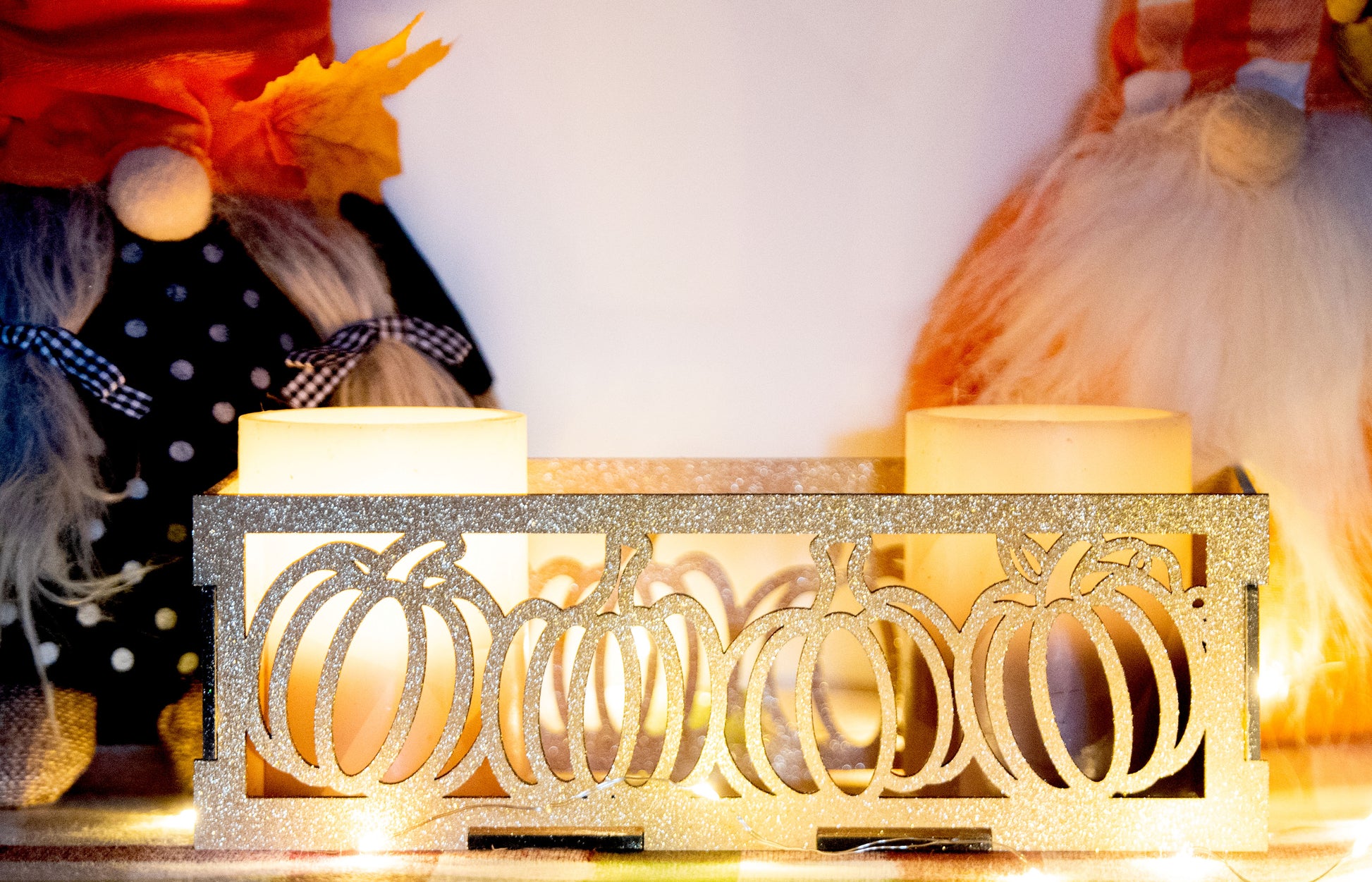 et of three intricately designed metal and wood pumpkin candle holders displayed on a checkered fall table runner. The set includes a tall rectangular lantern, a horizontal centerpiece tray, and a small square holder, each featuring layered pumpkin cutouts that beautifully glow with the warm light of tea candles inside—perfect for cozy fall, Thanksgiving, or farmhouse-style decor.