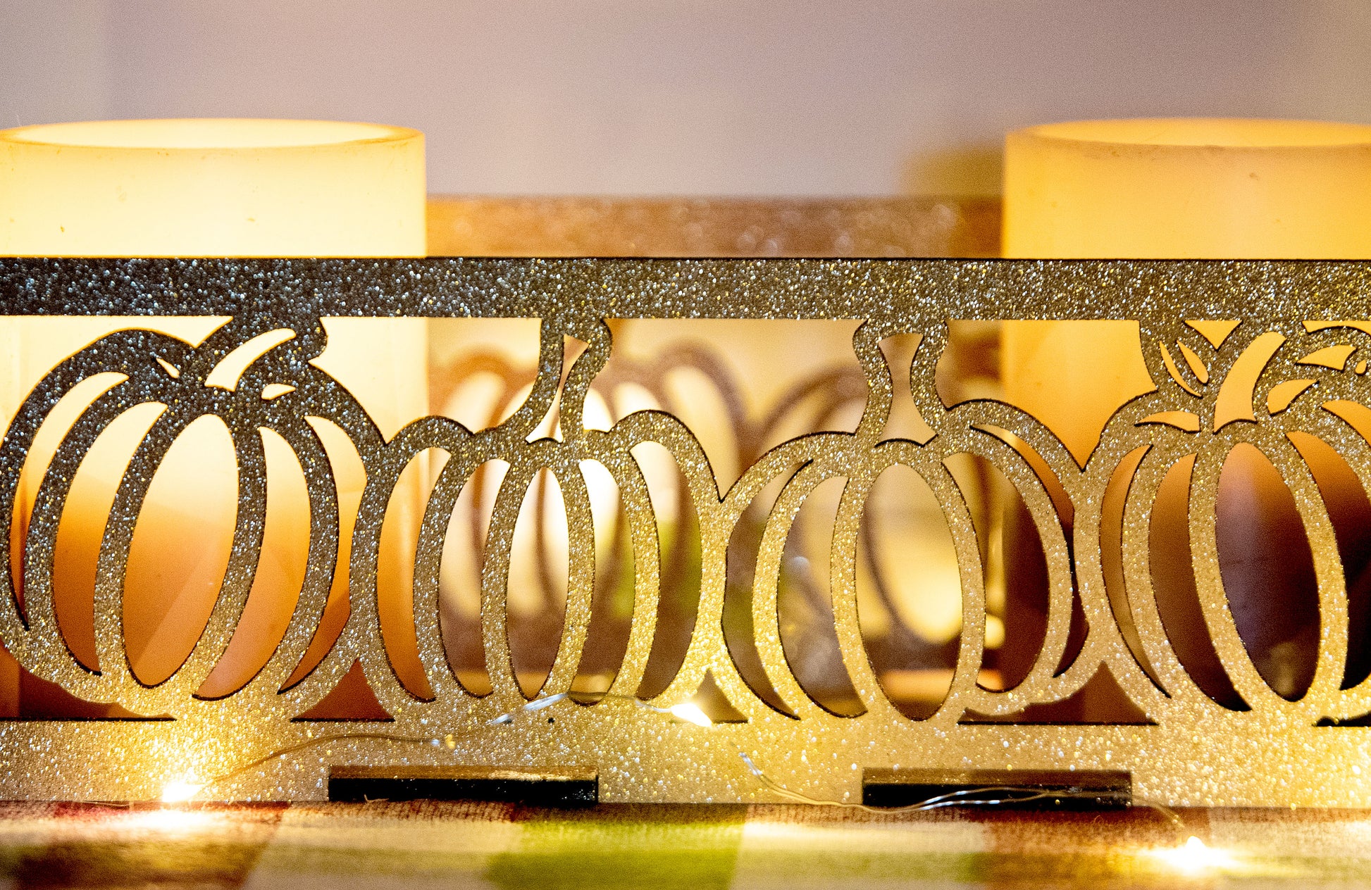 et of three intricately designed metal and wood pumpkin candle holders displayed on a checkered fall table runner. The set includes a tall rectangular lantern, a horizontal centerpiece tray, and a small square holder, each featuring layered pumpkin cutouts that beautifully glow with the warm light of tea candles inside—perfect for cozy fall, Thanksgiving, or farmhouse-style decor.
