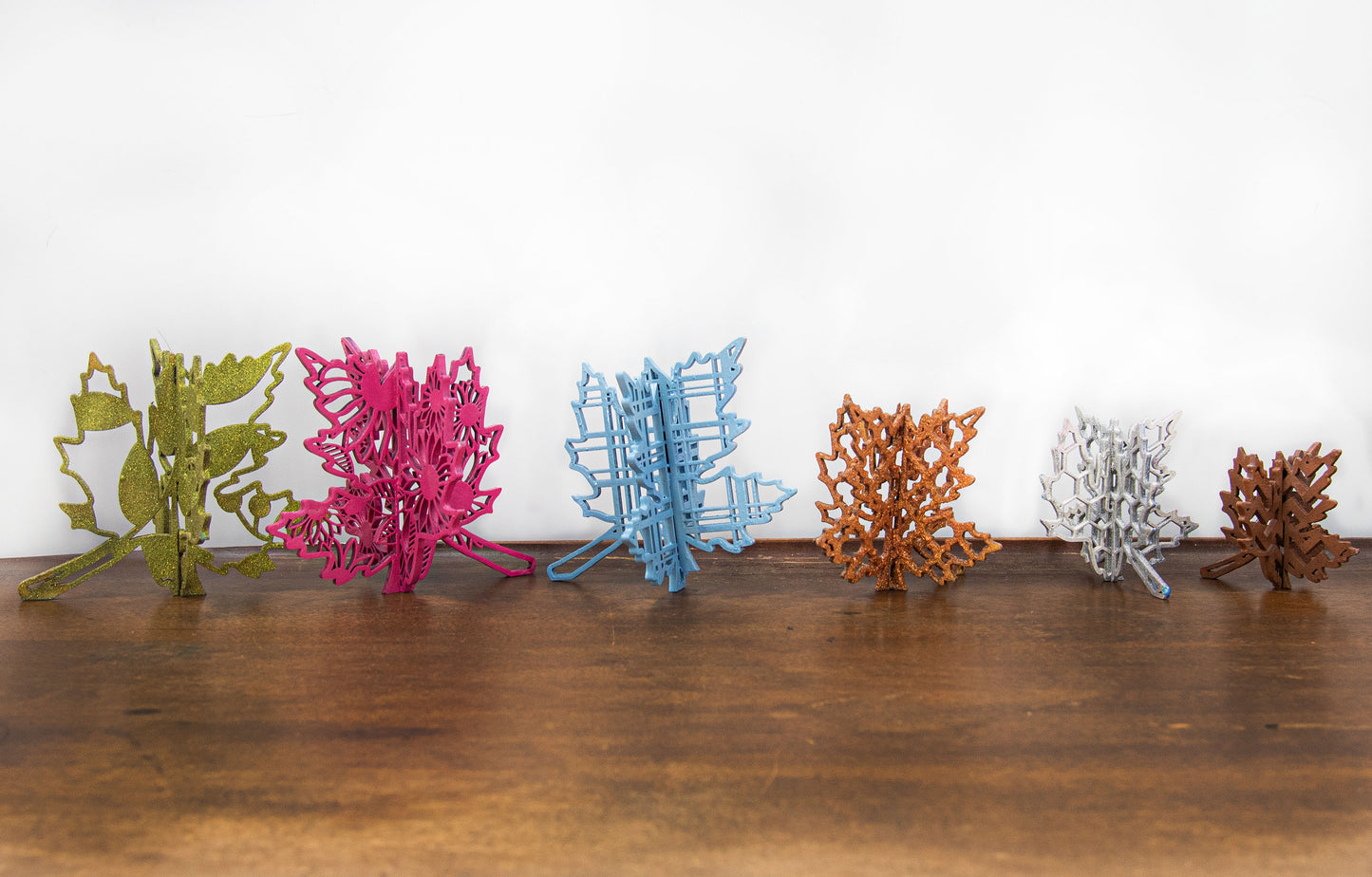 Freestanding 3D wooden leaf shelf sitters crafted with an interlocking two-piece design, painted in warm autumn colors such as orange, red, yellow, and brown. Each leaf features intricate engraved patterns and textures, making them perfect for seasonal tiered trays, mantels, or fall-themed centerpieces. Sizes range from 3 to 5.5 inches tall, with customizable color options for a unique, rustic autumn decor touch.
