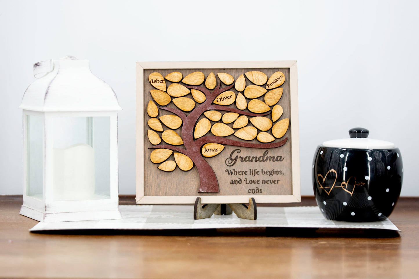 Square wooden framed family tree wall hanging featuring a carved tree trunk and branches with engraved wooden leaves for each child or grandchild’s name, rustic stained finish, and a heartfelt message for mom or grandma in the corne