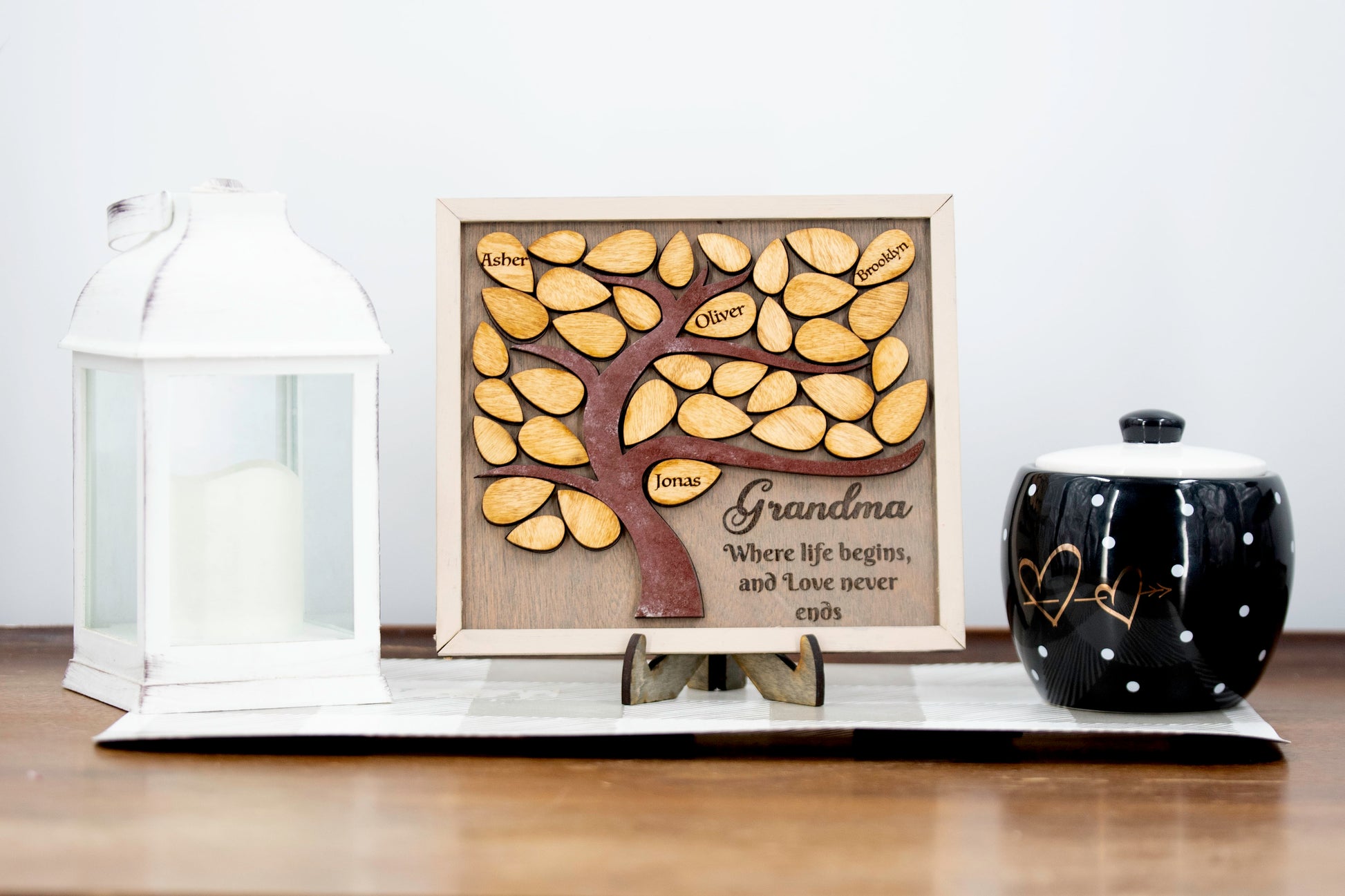 Square wooden framed family tree wall hanging featuring a carved tree trunk and branches with engraved wooden leaves for each child or grandchild’s name, rustic stained finish, and a heartfelt message for mom or grandma in the corne