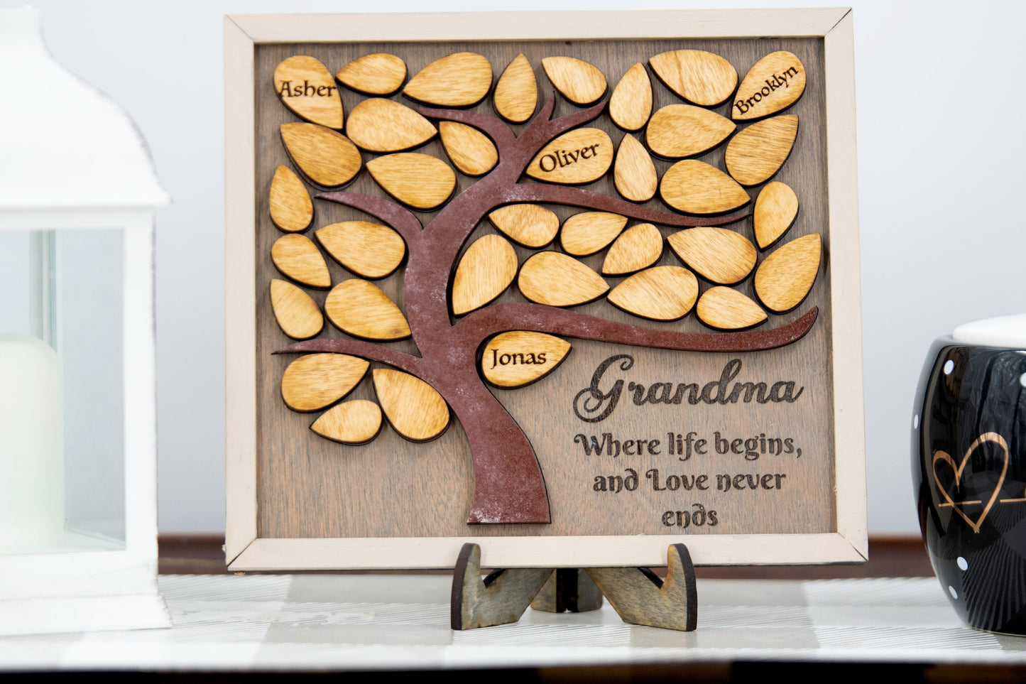 Square wooden framed family tree wall hanging featuring a carved tree trunk and branches with engraved wooden leaves for each child or grandchild’s name, rustic stained finish, and a heartfelt message for mom or grandma in the corne