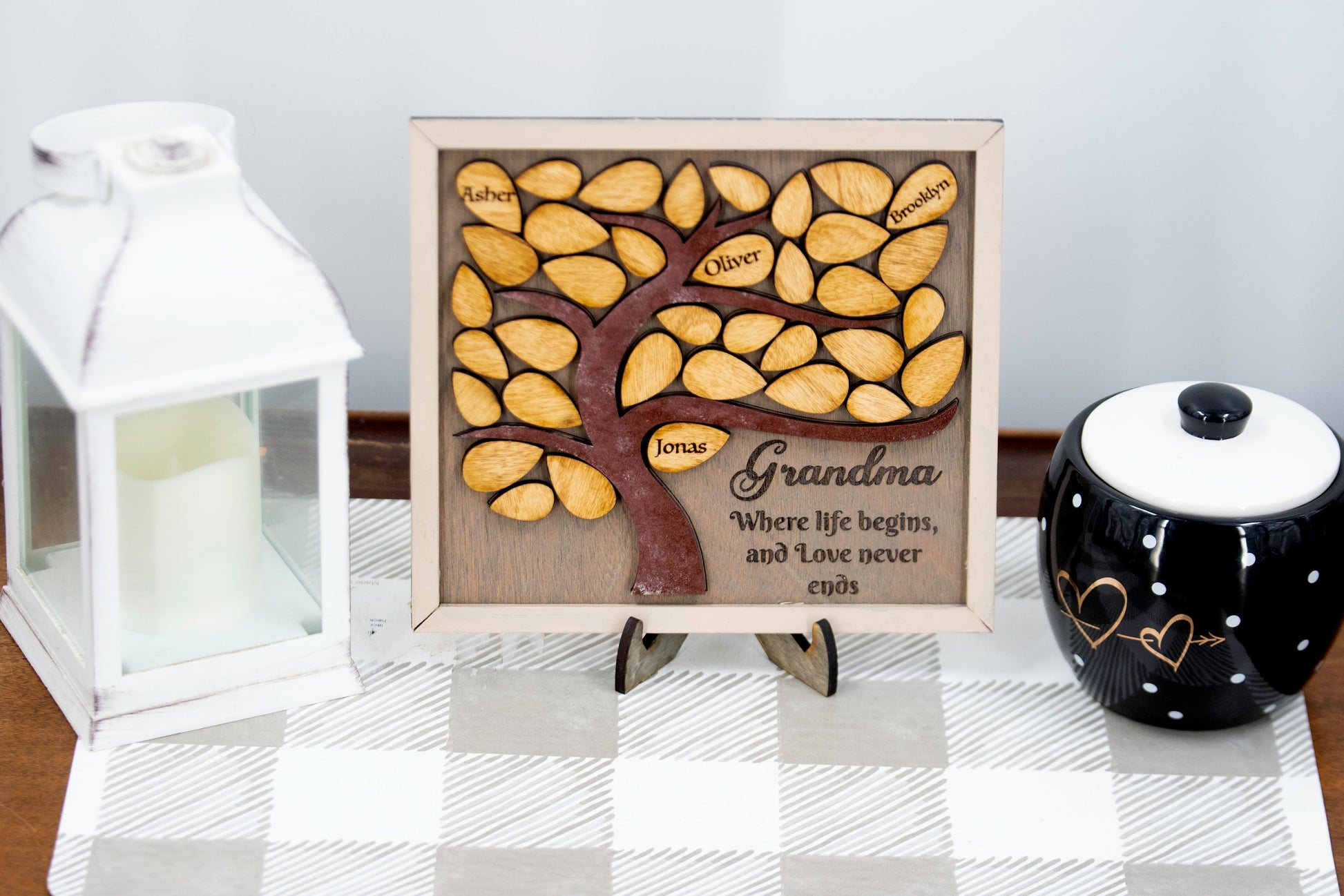 Square wooden framed family tree wall hanging featuring a carved tree trunk and branches with engraved wooden leaves for each child or grandchild’s name, rustic stained finish, and a heartfelt message for mom or grandma in the corne