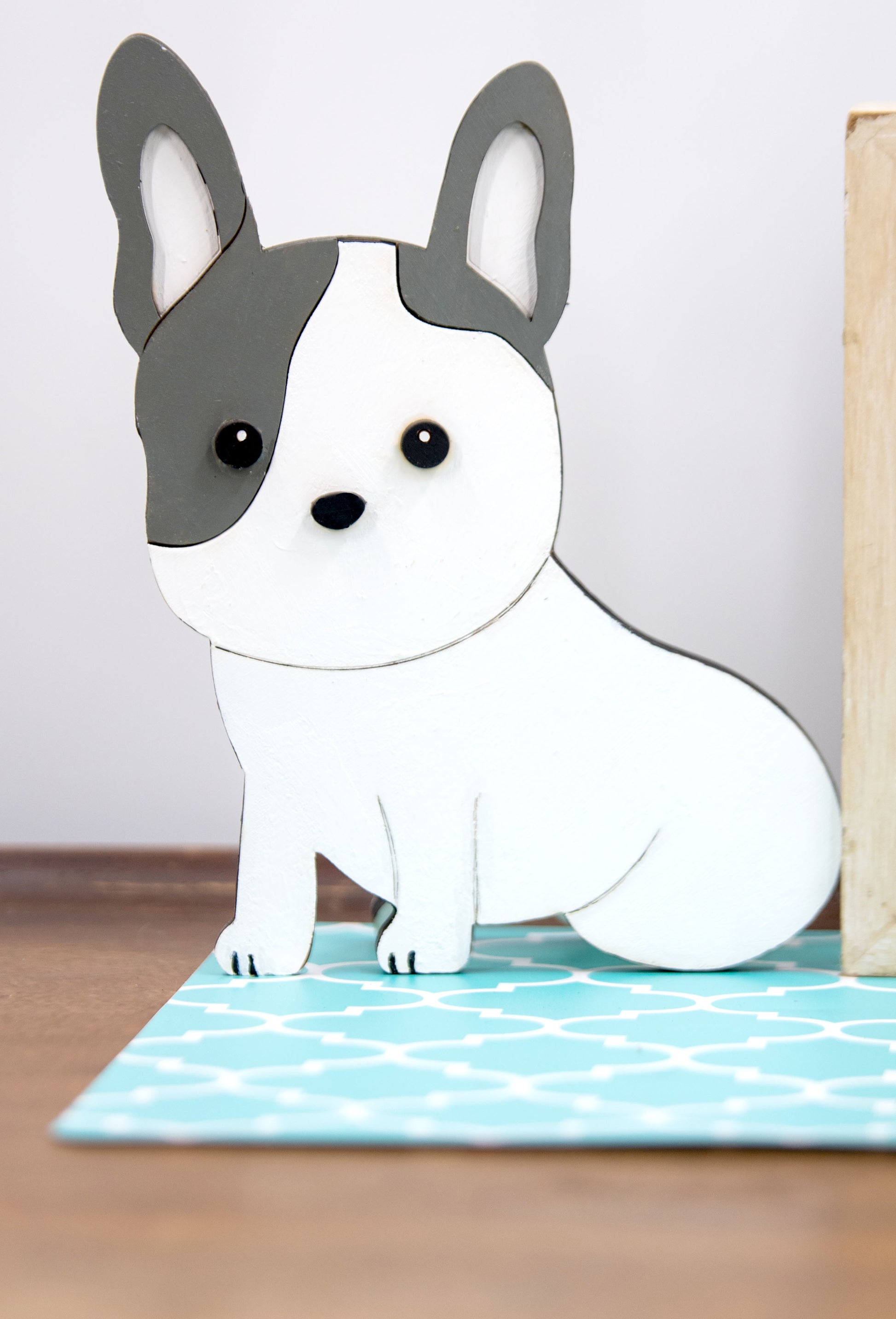 A hand-painted wooden glasses holder shaped like the face of a French Bulldog, featuring detailed ears, muzzle, and facial markings. The stand includes a flat base for stability and is designed to securely hold a pair of eyeglasses on the dog’s nose. Ideal as a decorative desk accessory, nightstand organizer, or pet-themed gift for Frenchie lovers.
