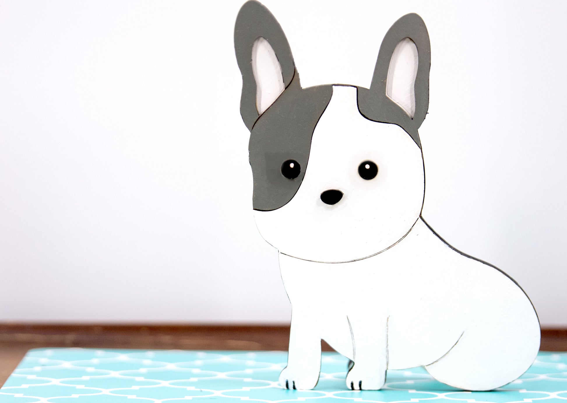 A hand-painted wooden glasses holder shaped like the face of a French Bulldog, featuring detailed ears, muzzle, and facial markings. The stand includes a flat base for stability and is designed to securely hold a pair of eyeglasses on the dog’s nose. Ideal as a decorative desk accessory, nightstand organizer, or pet-themed gift for Frenchie lovers.
