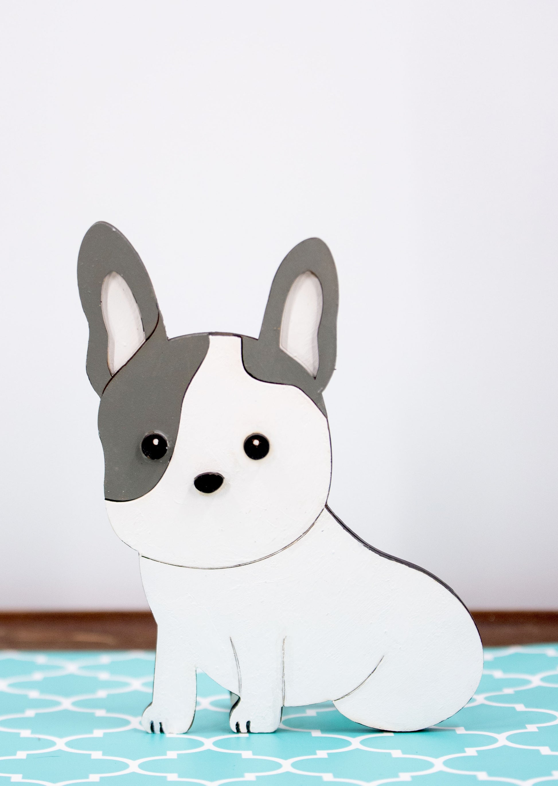 A hand-painted wooden glasses holder shaped like the face of a French Bulldog, featuring detailed ears, muzzle, and facial markings. The stand includes a flat base for stability and is designed to securely hold a pair of eyeglasses on the dog’s nose. Ideal as a decorative desk accessory, nightstand organizer, or pet-themed gift for Frenchie lovers.

