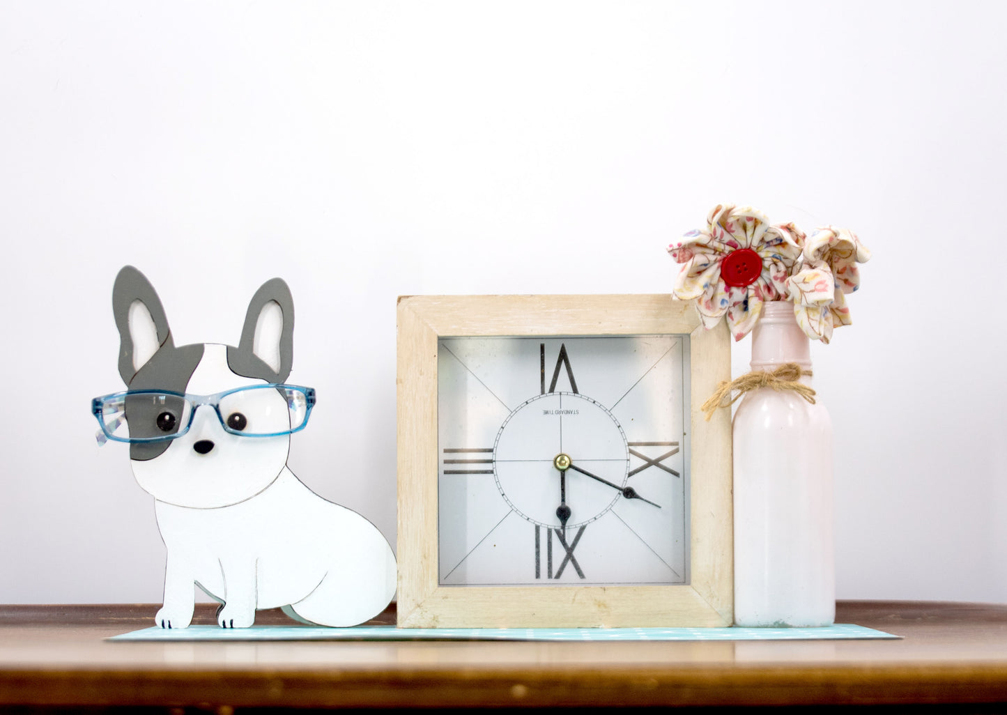 A hand-painted wooden glasses holder shaped like the face of a French Bulldog, featuring detailed ears, muzzle, and facial markings. The stand includes a flat base for stability and is designed to securely hold a pair of eyeglasses on the dog’s nose. Ideal as a decorative desk accessory, nightstand organizer, or pet-themed gift for Frenchie lovers.
