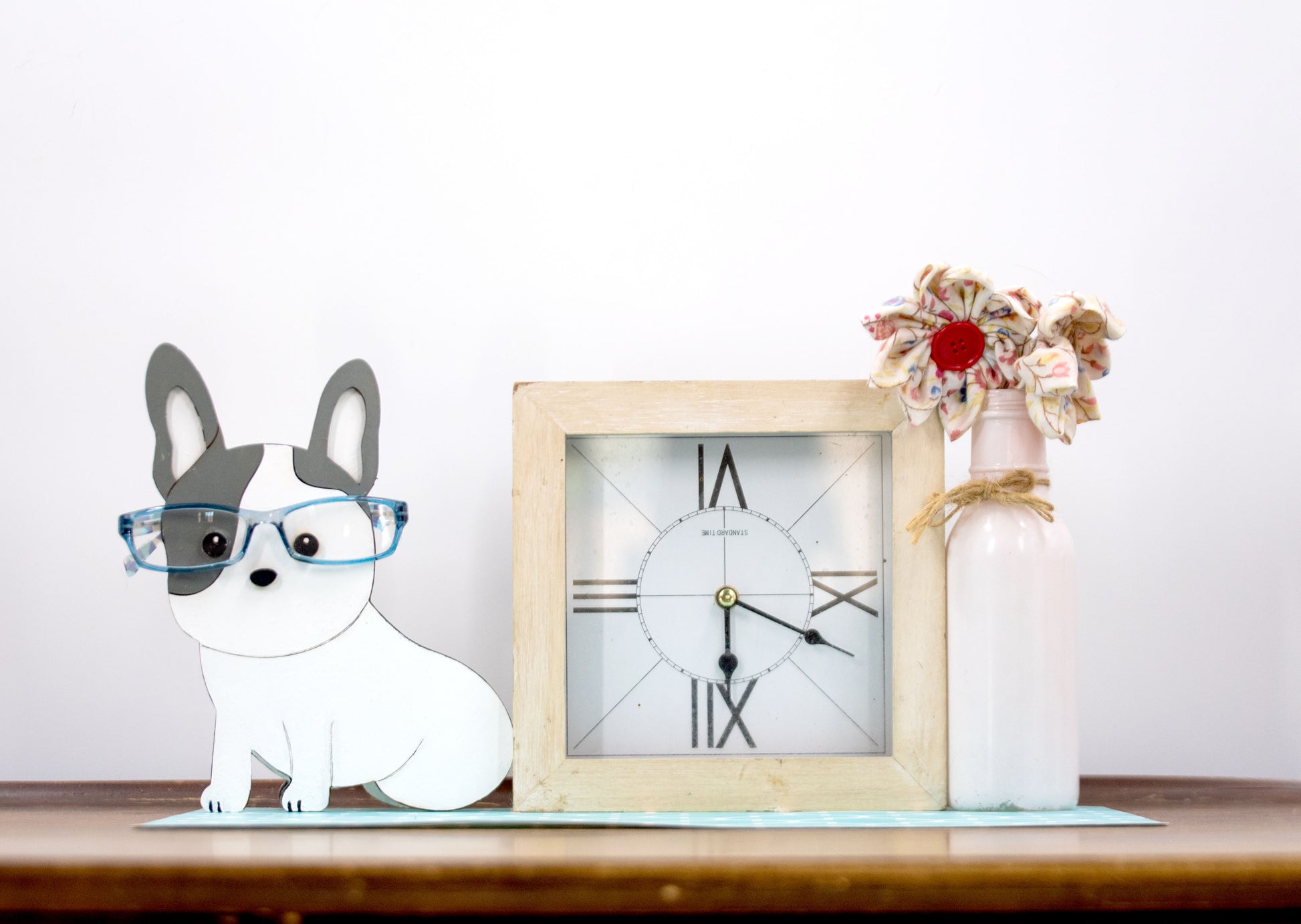 A hand-painted wooden glasses holder shaped like the face of a French Bulldog, featuring detailed ears, muzzle, and facial markings. The stand includes a flat base for stability and is designed to securely hold a pair of eyeglasses on the dog’s nose. Ideal as a decorative desk accessory, nightstand organizer, or pet-themed gift for Frenchie lovers.
